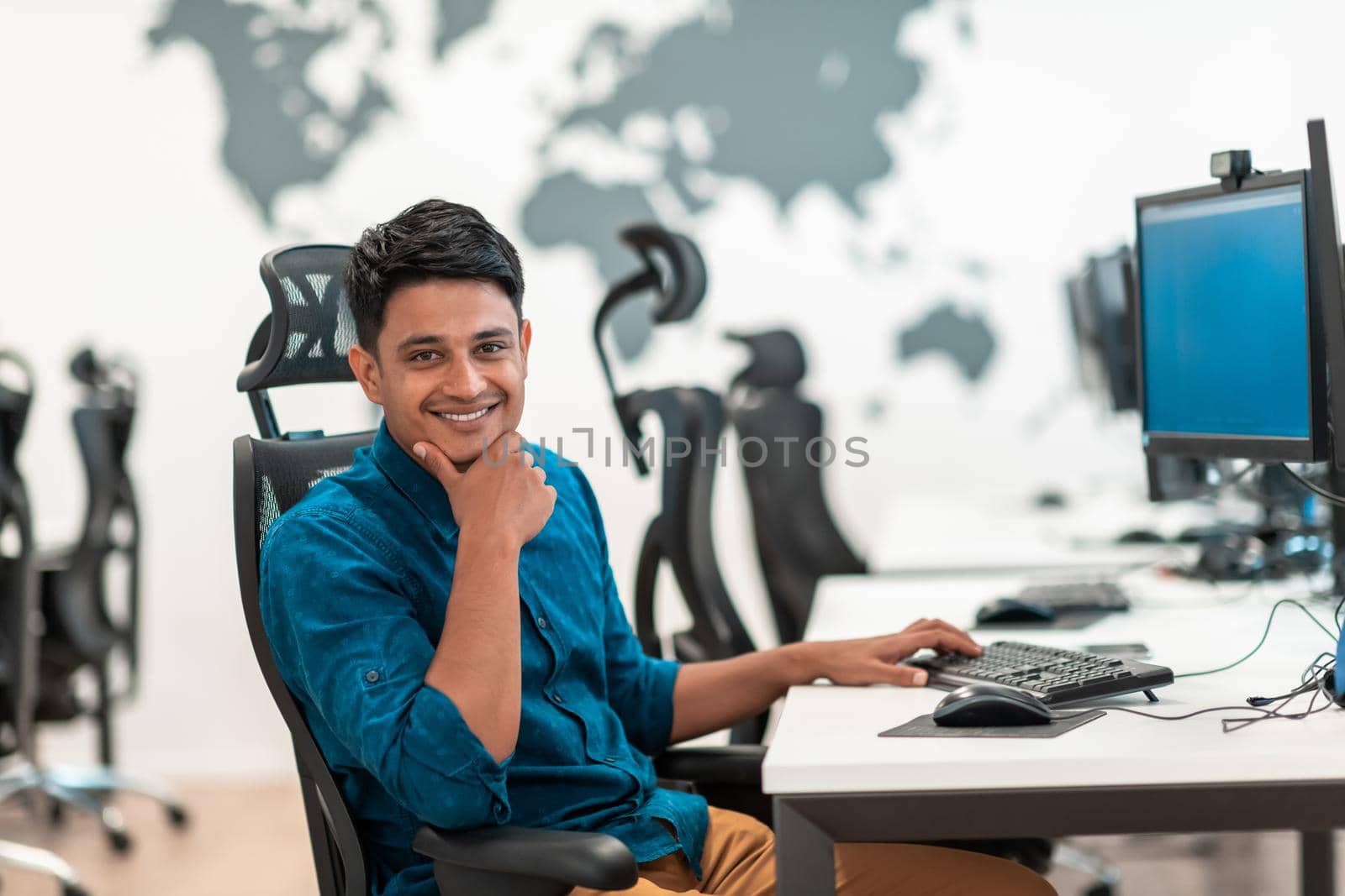 Casual businessman working on a desktop computer in modern open plan startup office interior. Selective focus. High-quality photo