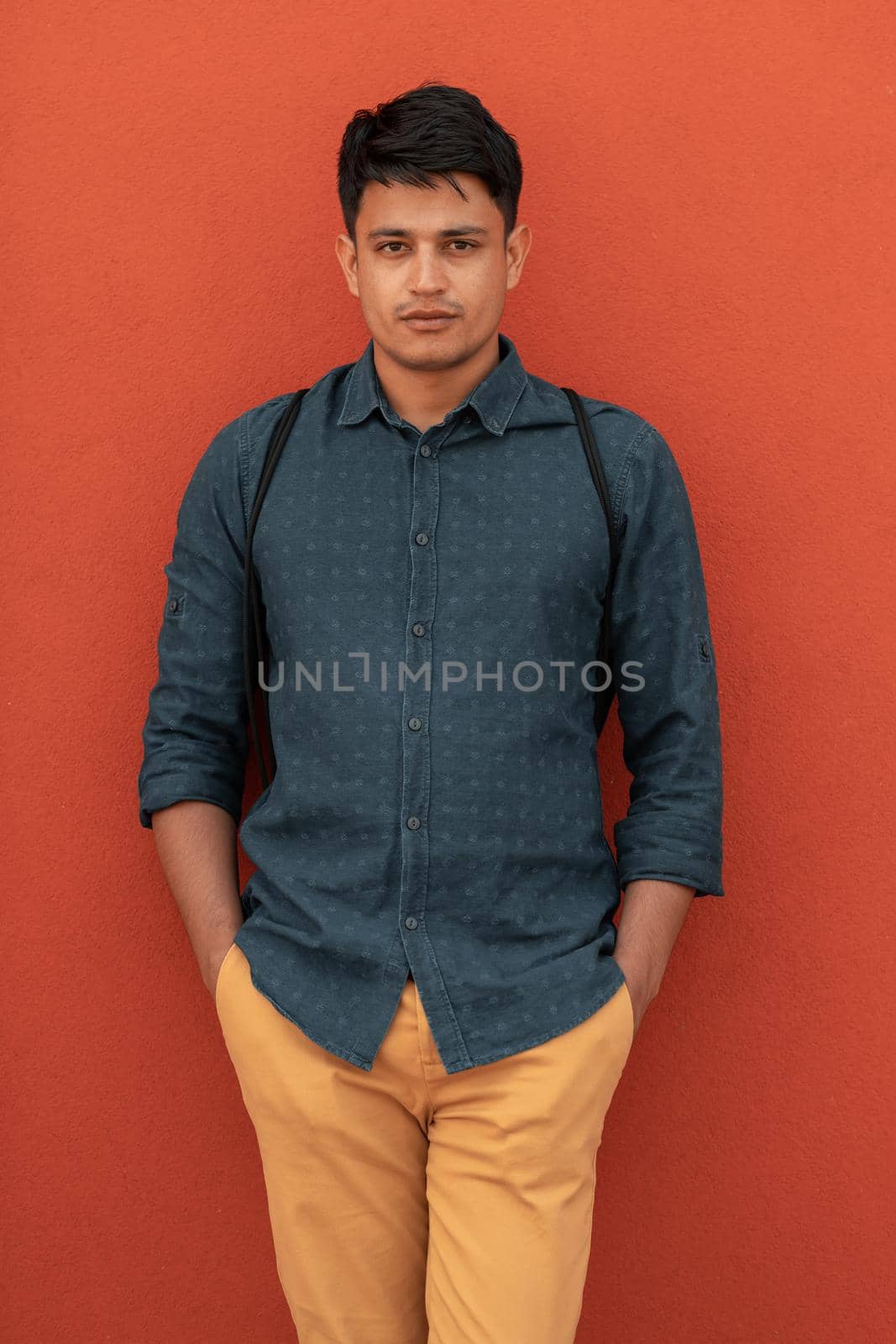 Startup business portrait of casual businessman with a blue shirt and backpack in front of a red wall. High-quality photo