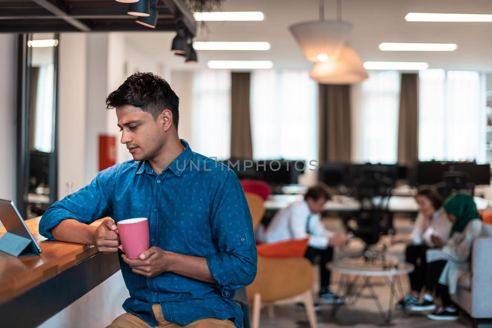 Casual businessman taking a break from the work using a laptop while drinking tea in relaxation area of modern open plan startup office. High-quality photo