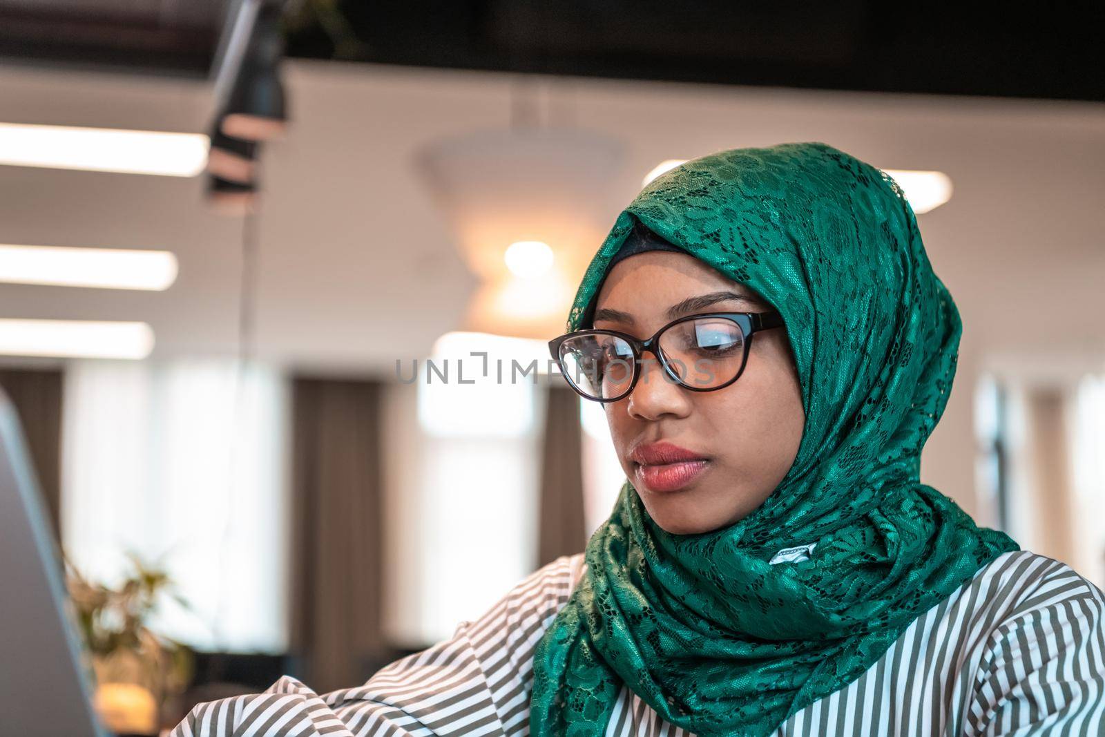 Businesswoman wearing a green hijab using laptop in relaxation area at modern open plan startup office. Selective focus. High-quality photo