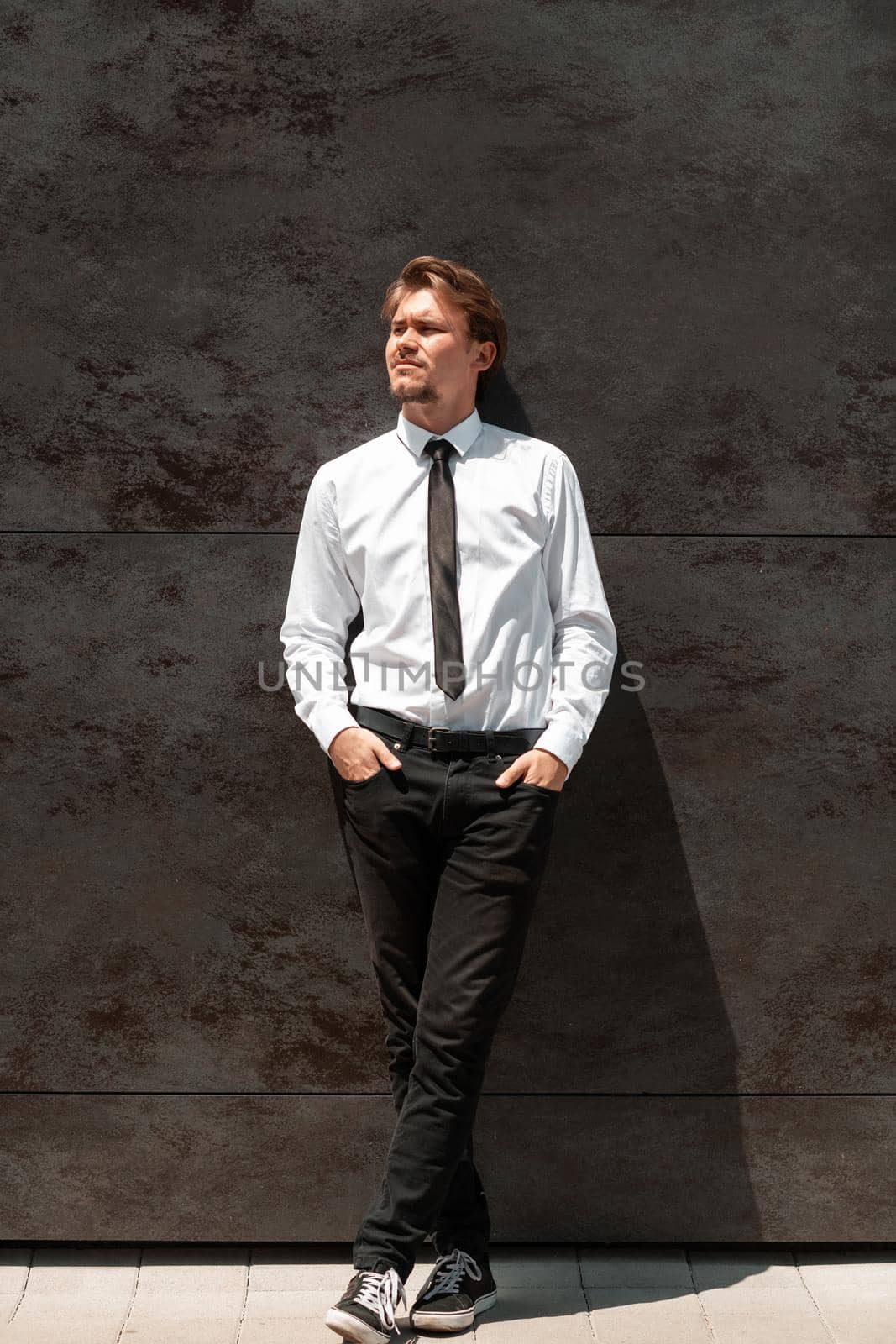 Portrait of startup businessman in a white shirt with a black tie standing in front of gray wall outside by dotshock