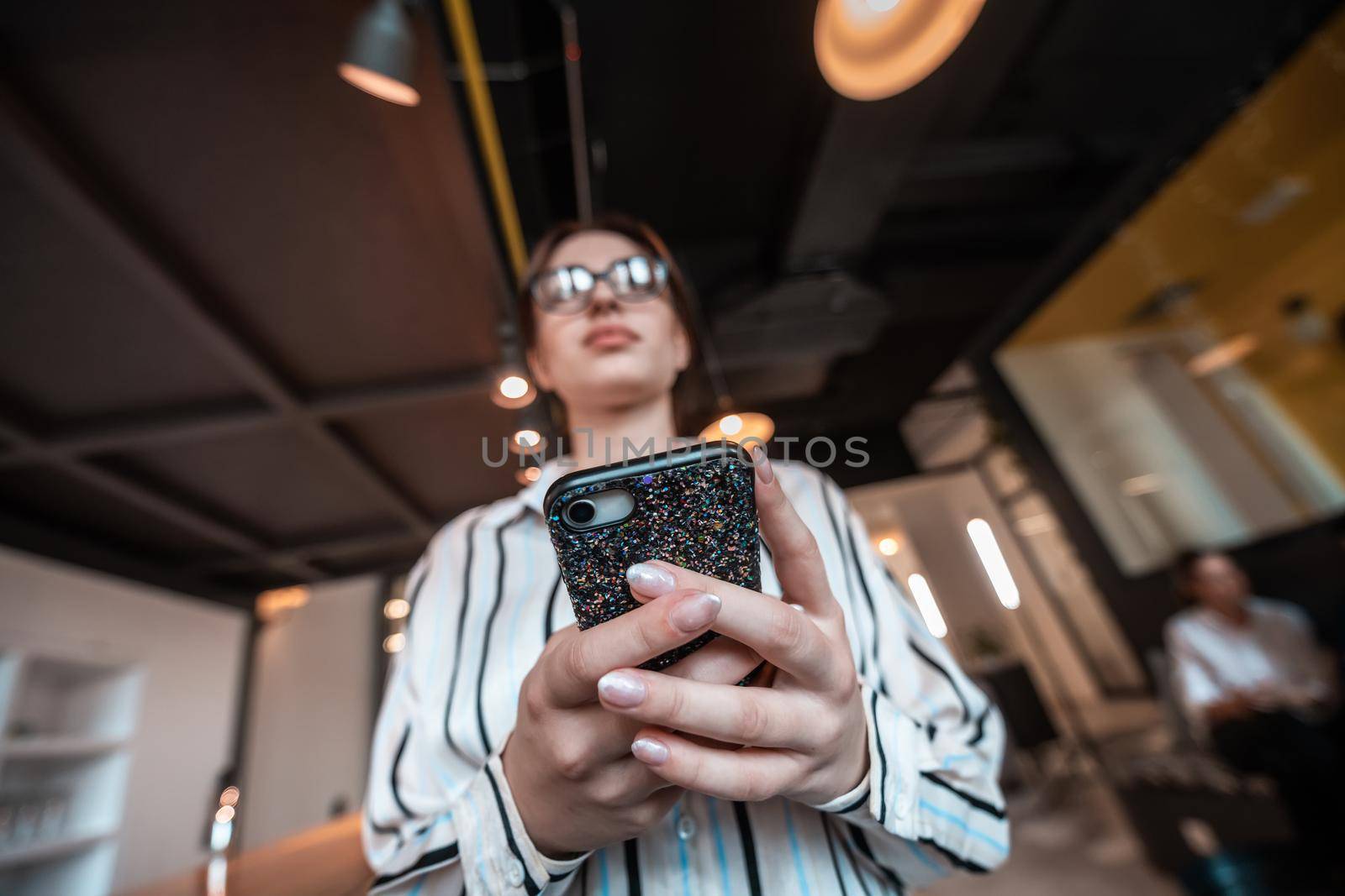 Businesswoman with glasses using mobile phone at modern startup open plan office interior. Selective focus by dotshock