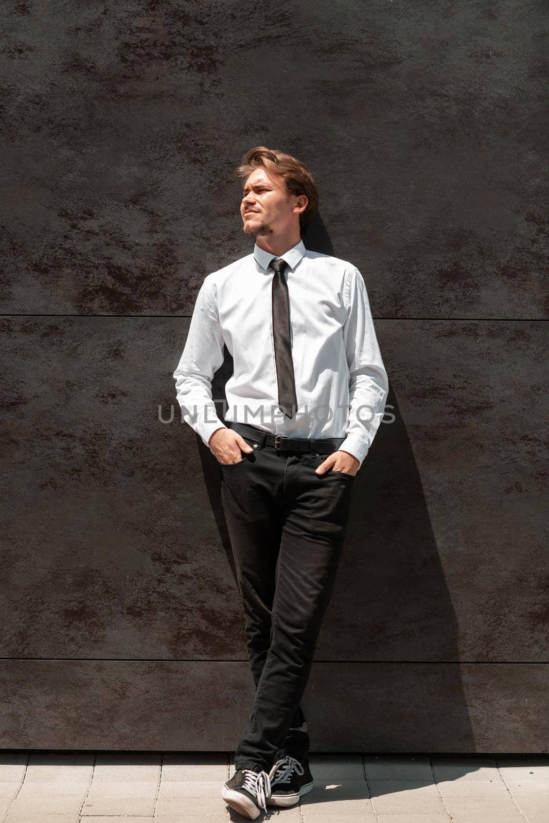 Portrait of startup businessman in a white shirt with a black tie standing in front of gray wall outside by dotshock