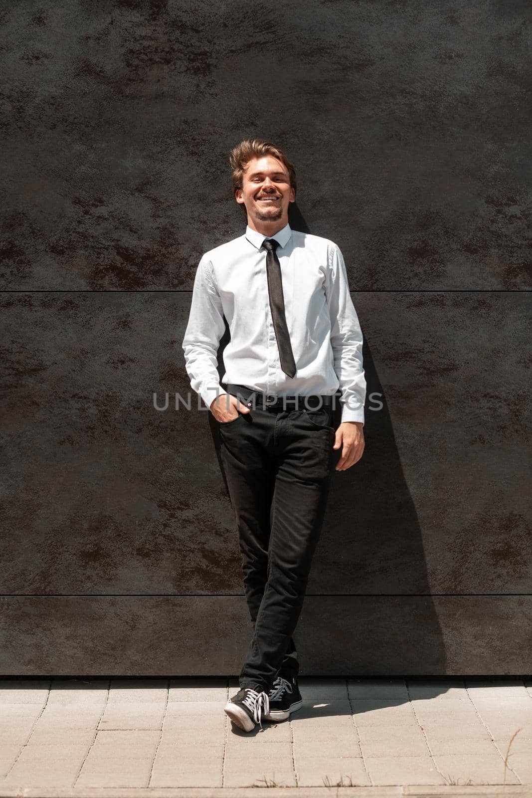 Portrait of startup businessman in a white shirt with a black tie standing in front of gray wall outside by dotshock