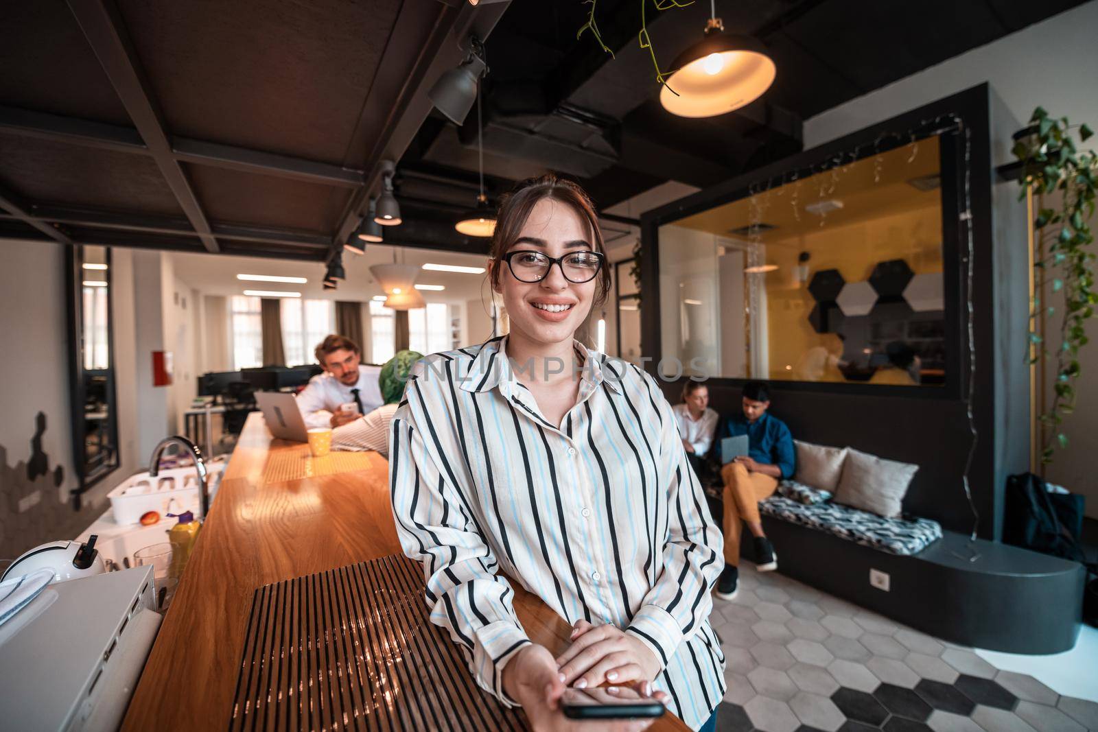 Businesswoman with glasses using a smartphone at modern startup open plan office interior. Selective focus. High-quality photo