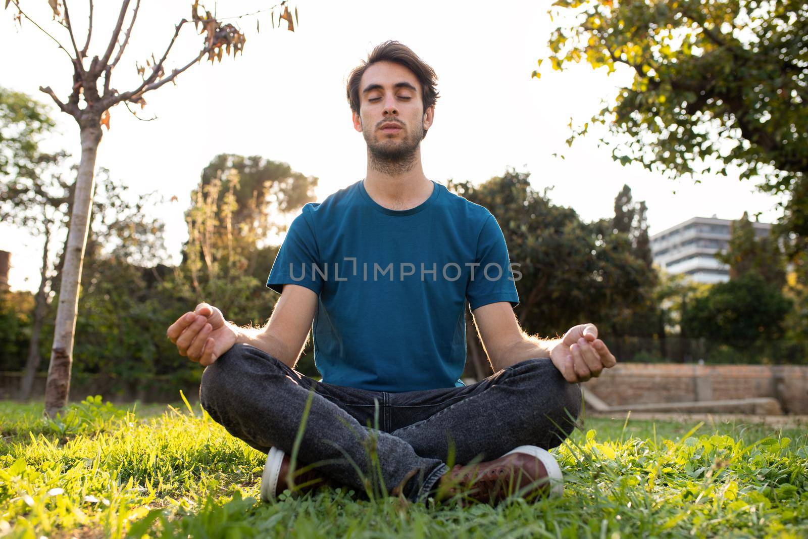 Front view of young caucasian man meditating in a park in the city. Copy space. Spirituality and mindfulness concept.