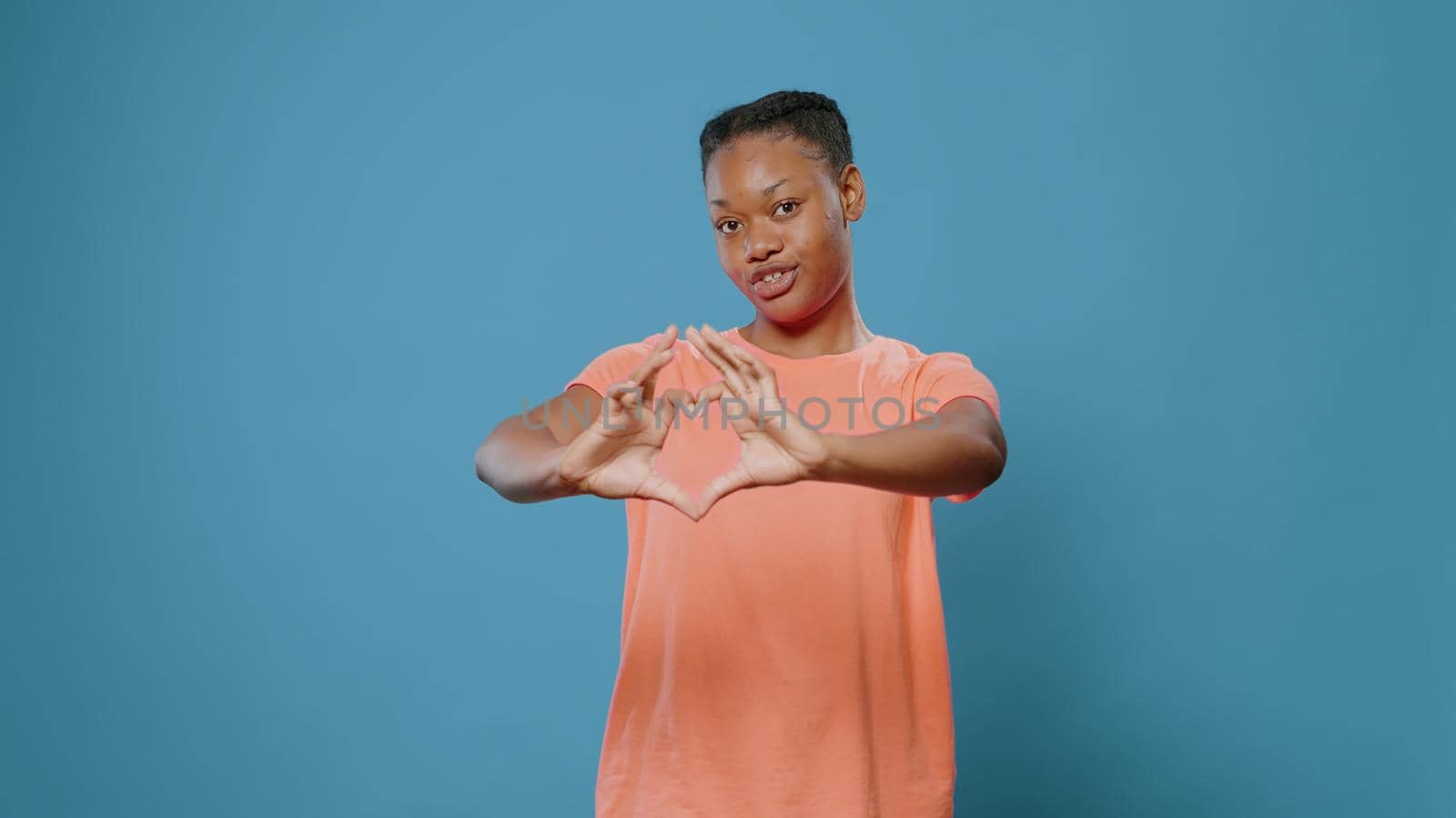 Young woman doing heart shape symbol with hands in studio. Affectionate person showing love sign and romantic gesture, expressing feelings and affection, standing over isolated background.
