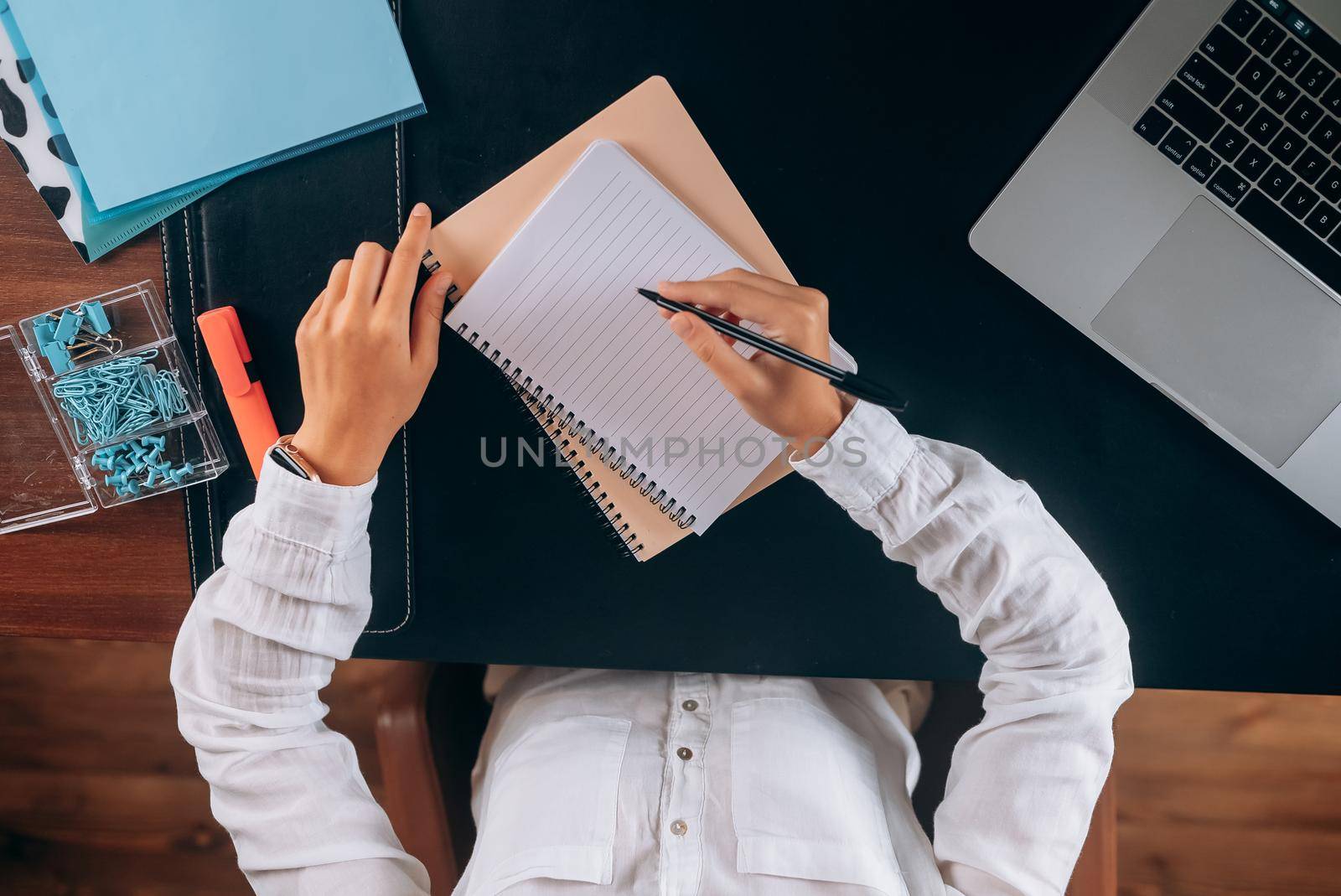 A woman's hand writing down on a white blank notebook on table.
