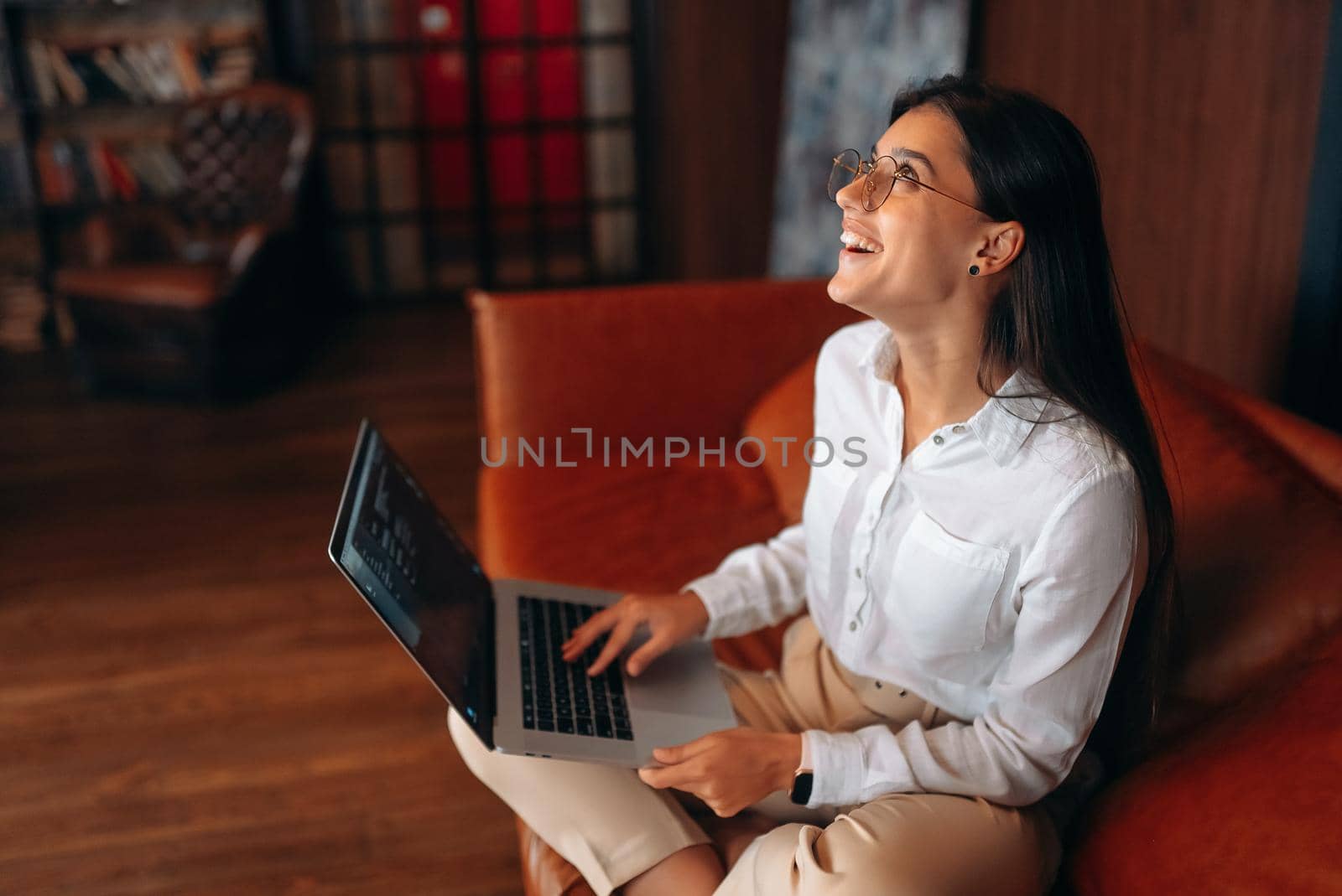 Young woman sits on a red sofa while working at a laptop. Woman hands typing on laptop keyboard.