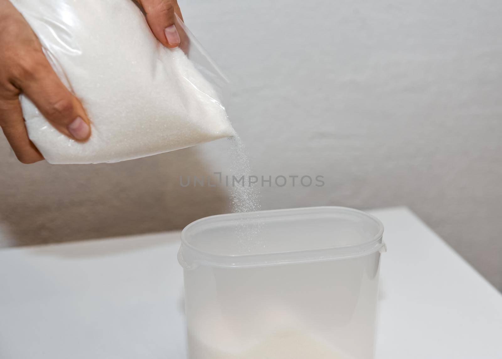 Storing sugar at home, arranging a place in the kitchen. Pouring sugar from a bag into a plastic container.