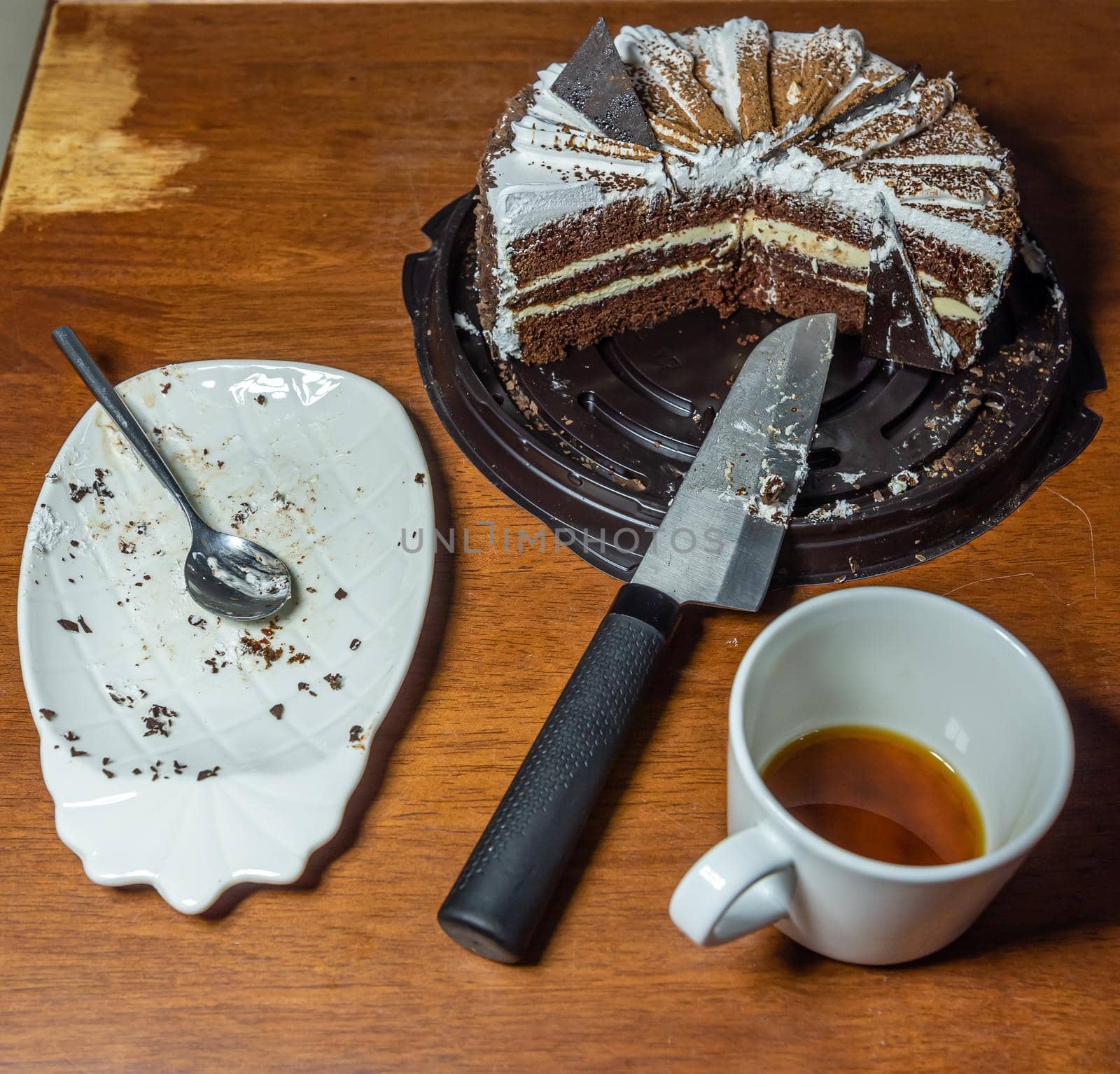 White plate with crumbs and a spoon after the cake, drinking a cup of coffee and a cut cake on a wooden table, top view.