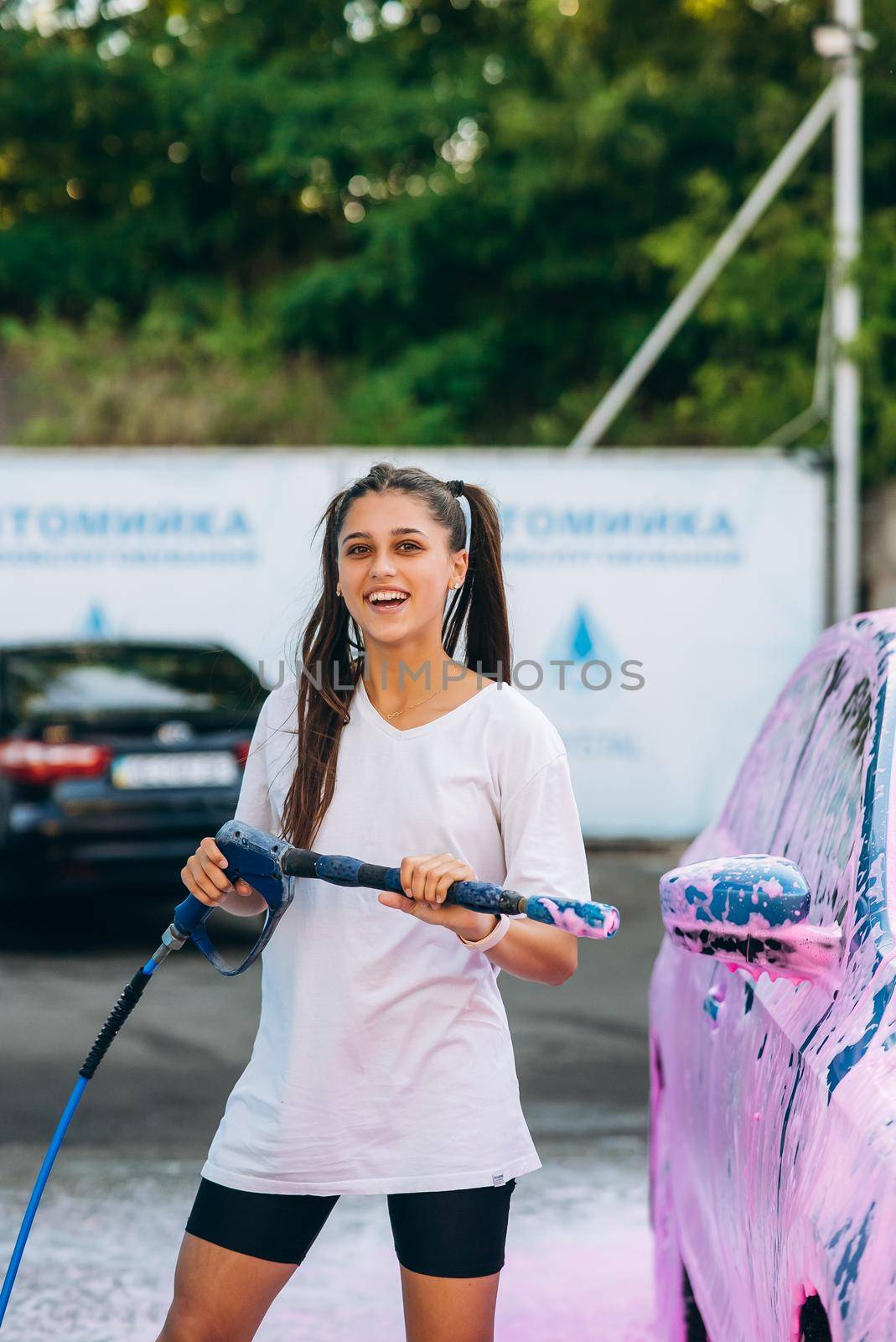 Woman with high pressure hose stands by car