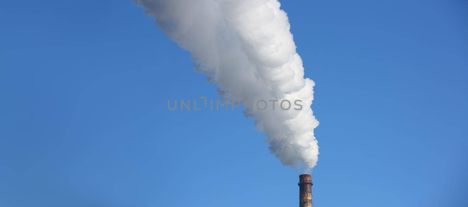 Chimney blows white smoke into blue sky. Air pollution from an industrial chimney