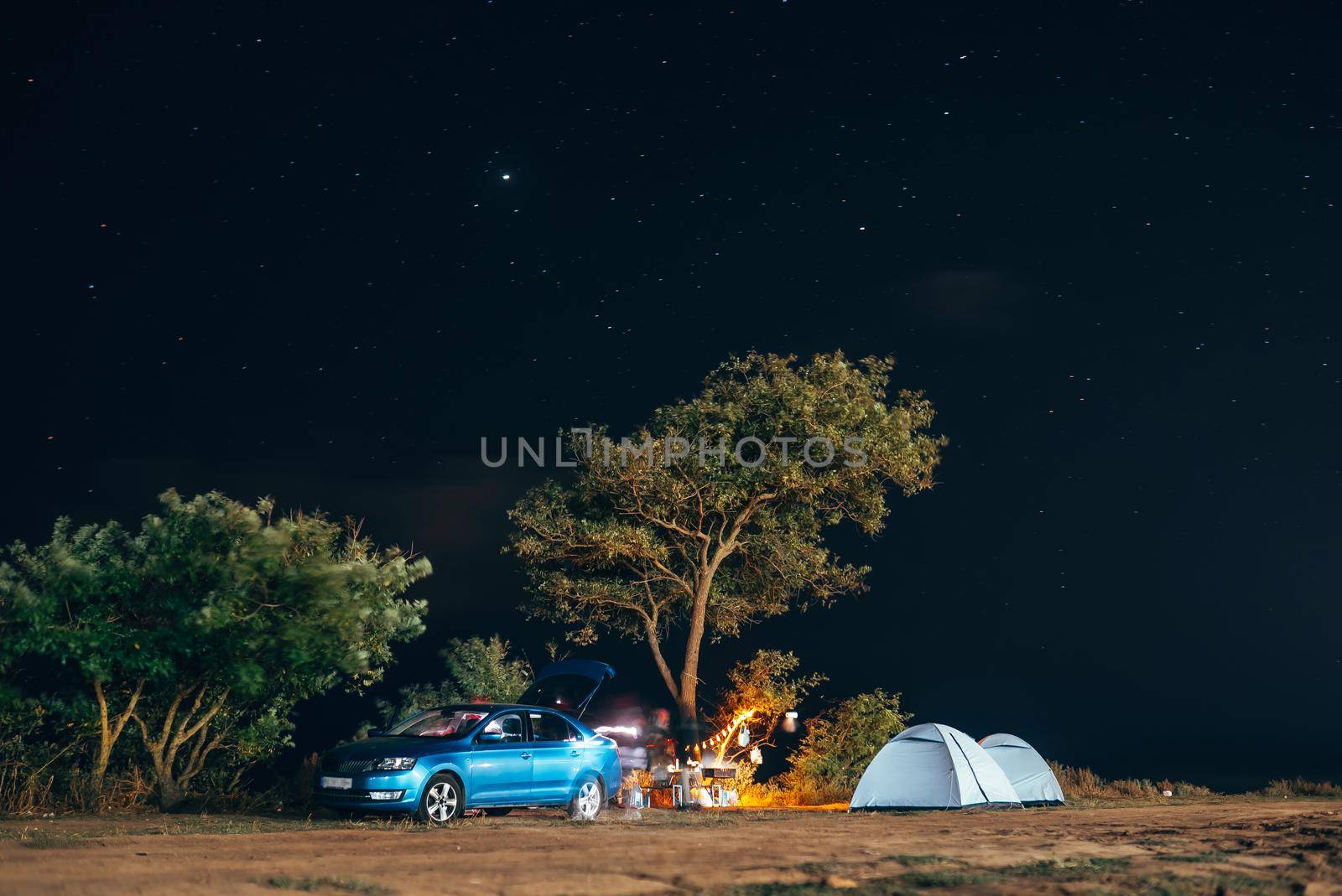 Group of five travellers rest on sea shore under tree on blue evening sky background. Tourism and camping concept.