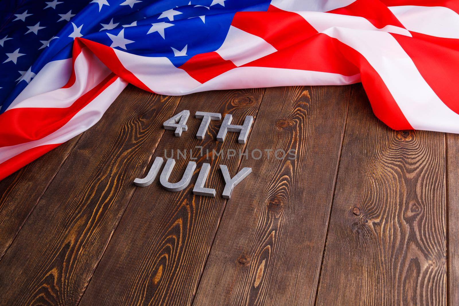the words 4th july and crumpled usa flag on flat textured wooden surface background.