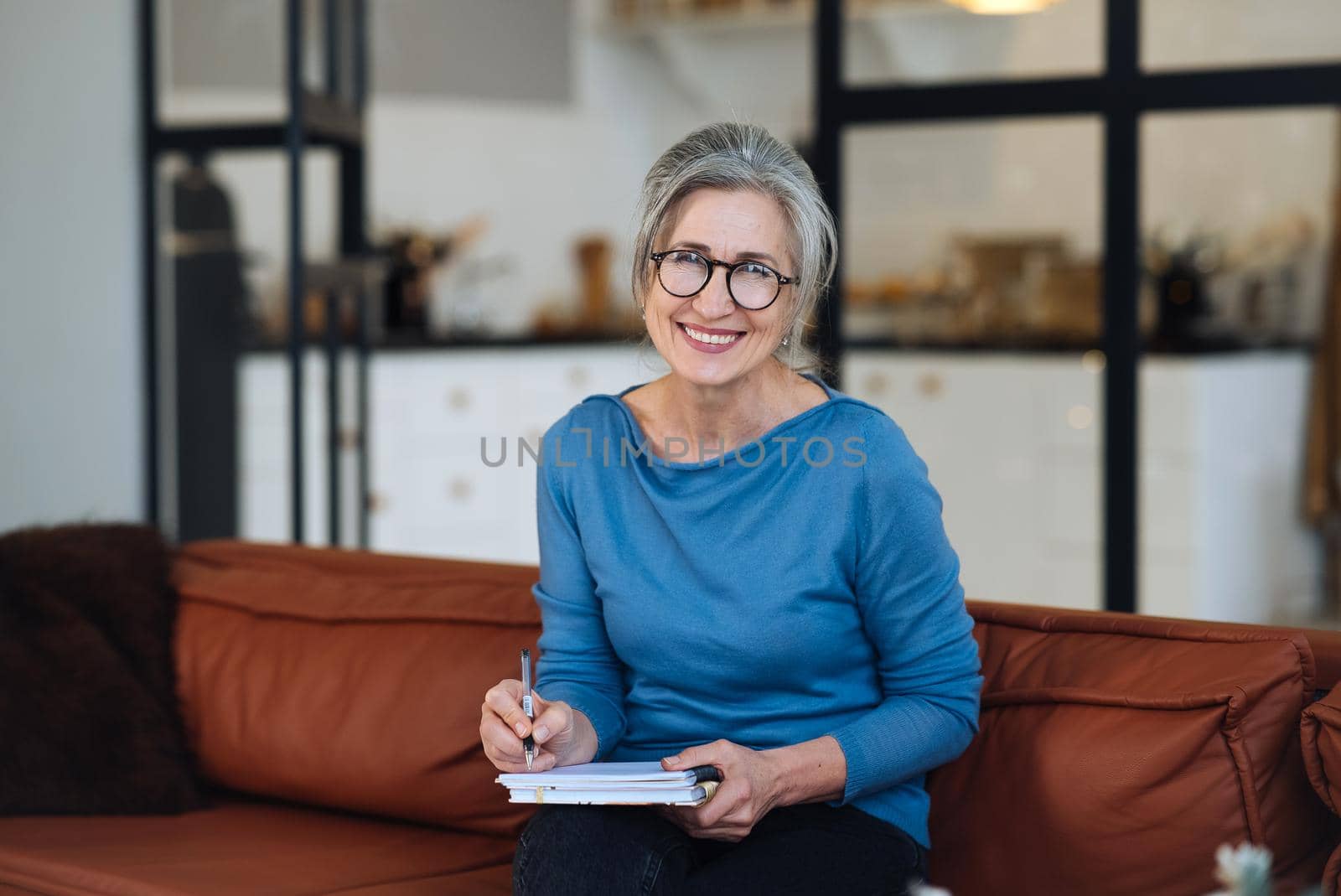 Happy senior woman in glasses writing to notebook or diary at home