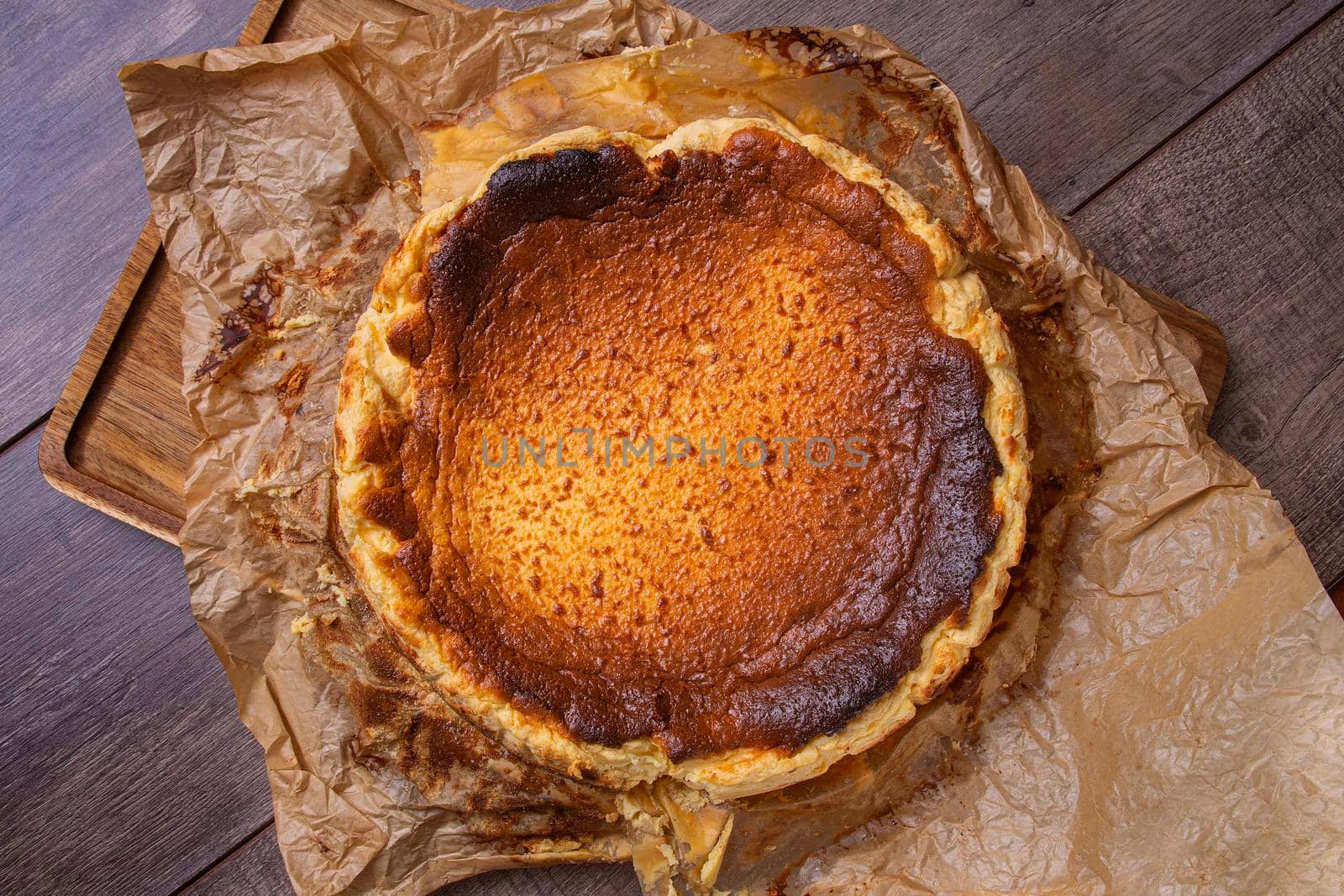 Top view of a still life of a cheesecake fresh from the oven on brown paper and wooden board. Concept of traditional Spanish gastronomy.