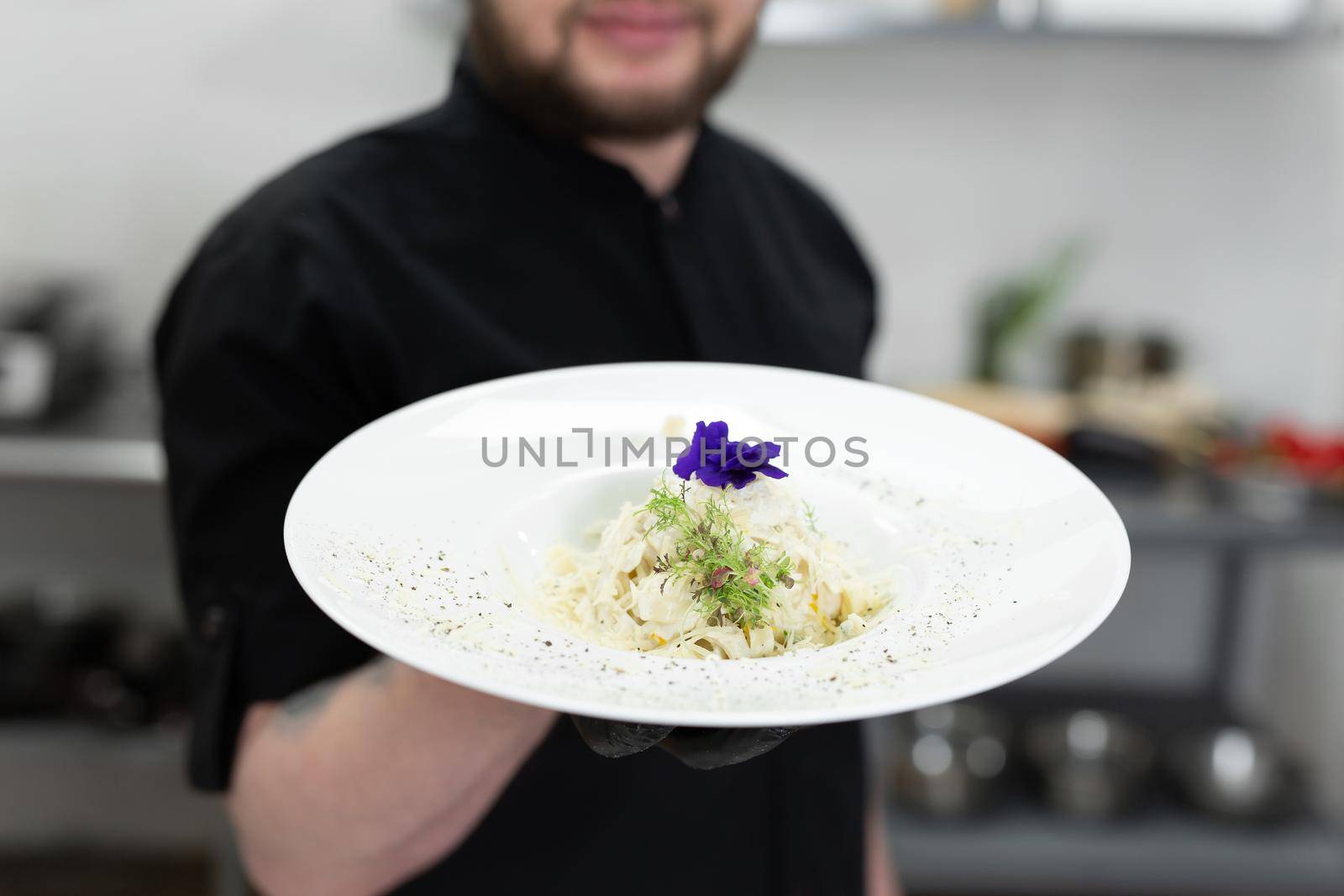 Chef presenting pasta dish in Italian restaurant kitchen.