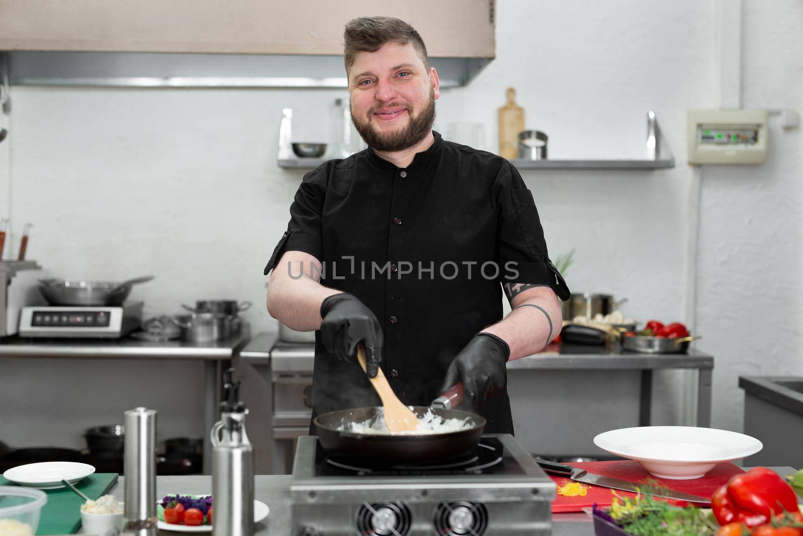 Male chef in a black uniform cooks pasta with cream and bacon in a frying pan by StudioPeace