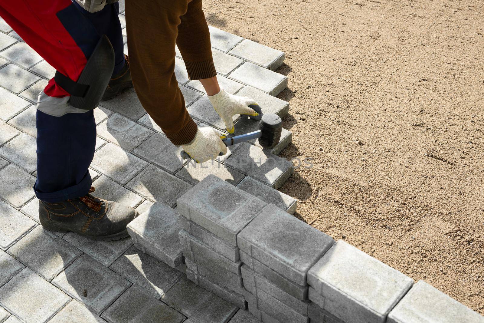 Hands of a worker installing concrete blocks, paving slabs with a rubber hammer.