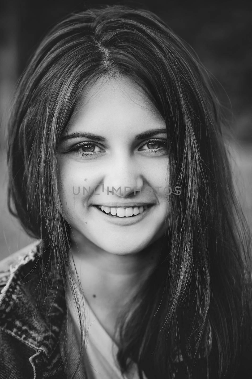 black and white portrait of a smiling teenage girl with long hair on a nature background