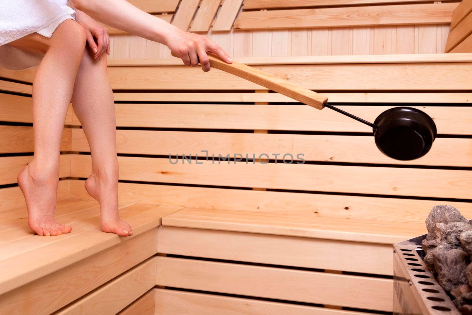 Woman pours water on a stones in a stove with a ladle. Traditional sauna.
