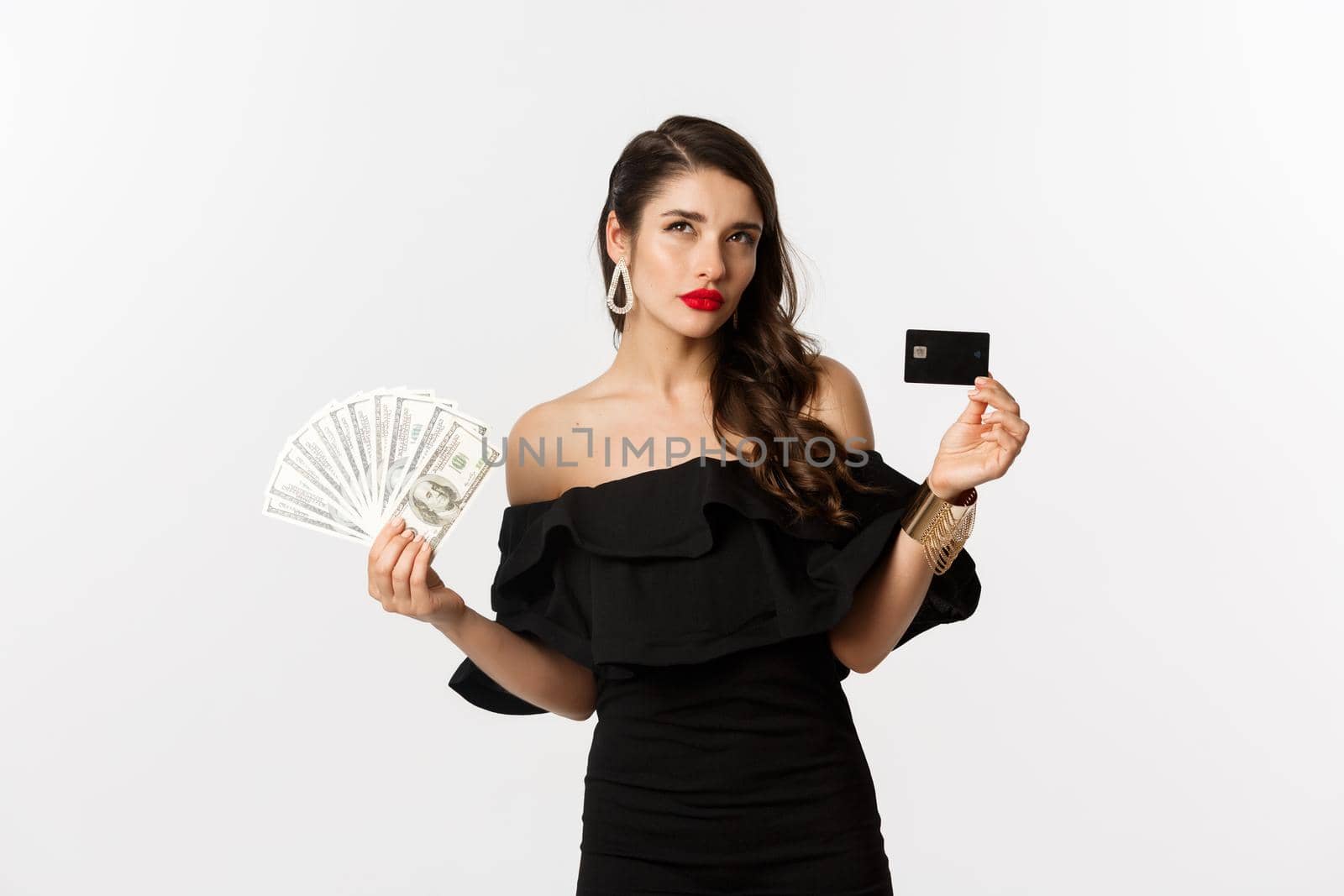 Fashion and shopping concept. Thoughtful woman holding credit card and dollars, thinking and looking up, white background.