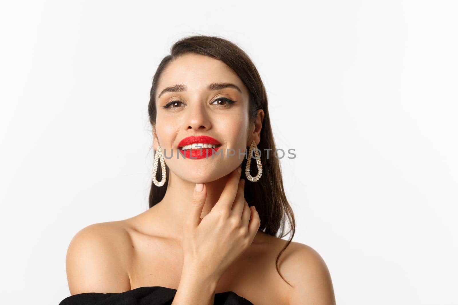 Fashion and beauty concept. Close-up of gorgeous brunette woman with red lips, touching face and smiling self-assured, standing over white background by Benzoix
