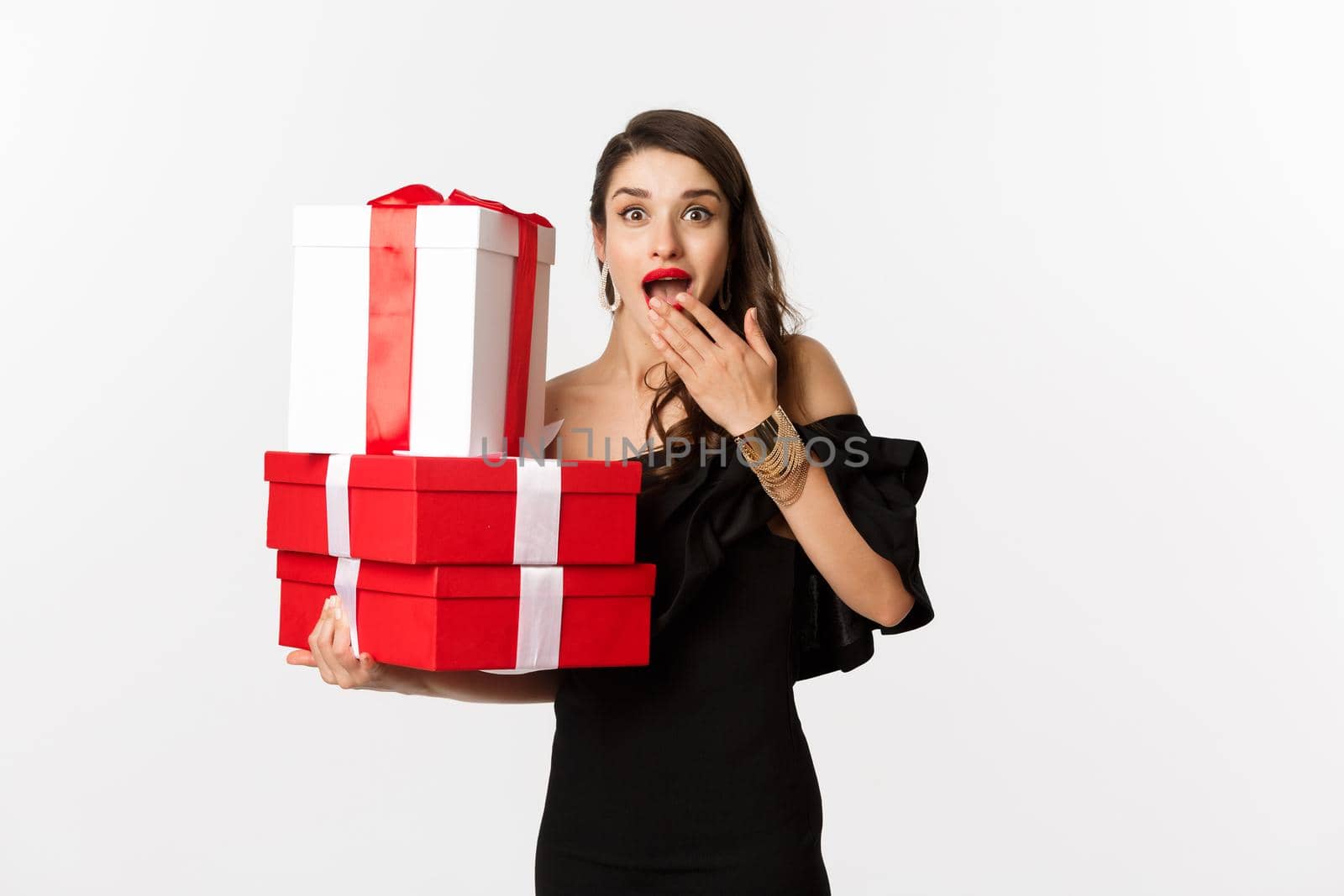 Celebration and christmas holidays concept. Woman holding xmas gifts and looking surprised, receive presents, standing over white background by Benzoix