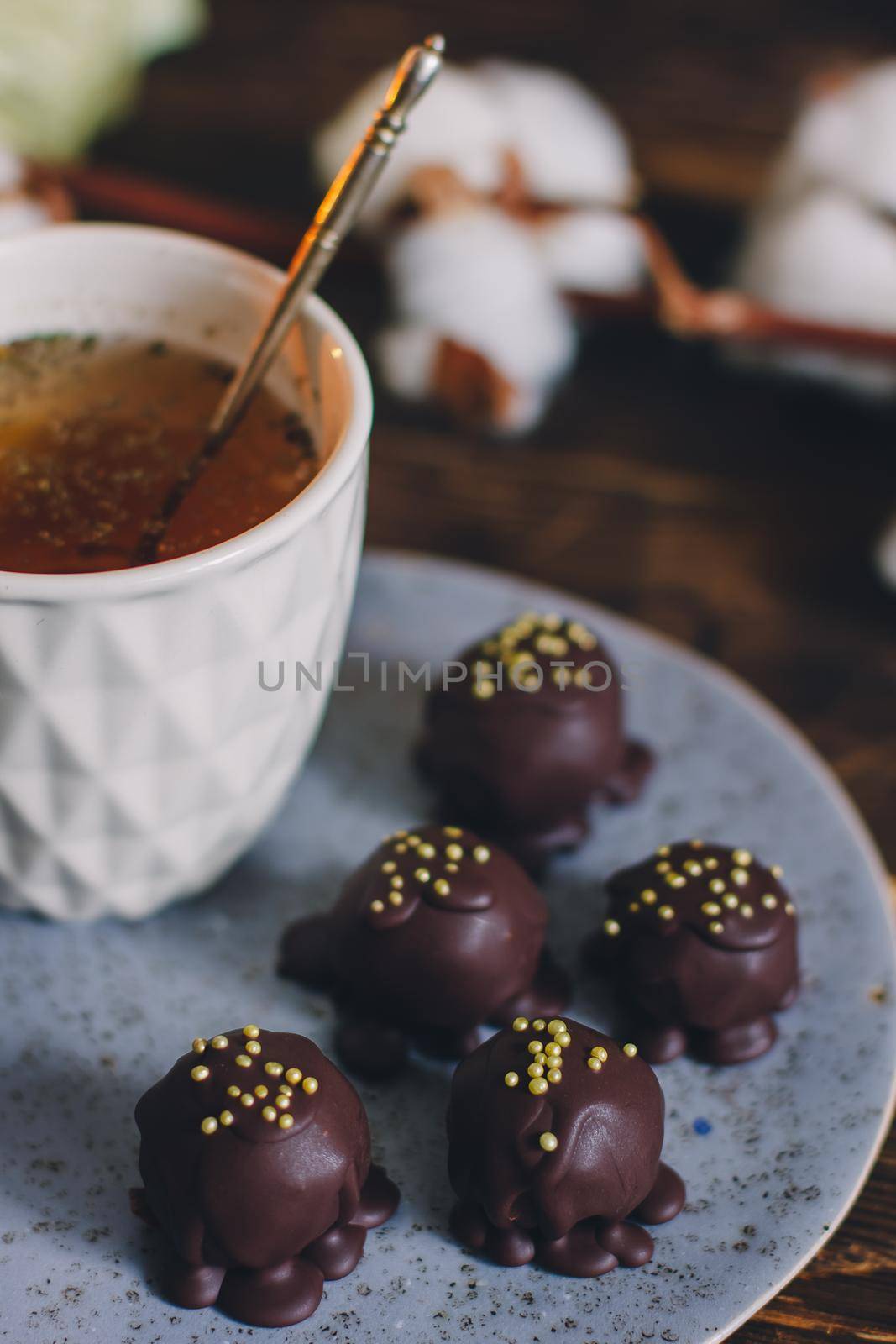 Dark chocolate handmade candy balls on handmade plate on dark wooden background with the cup of tea in a white cup.