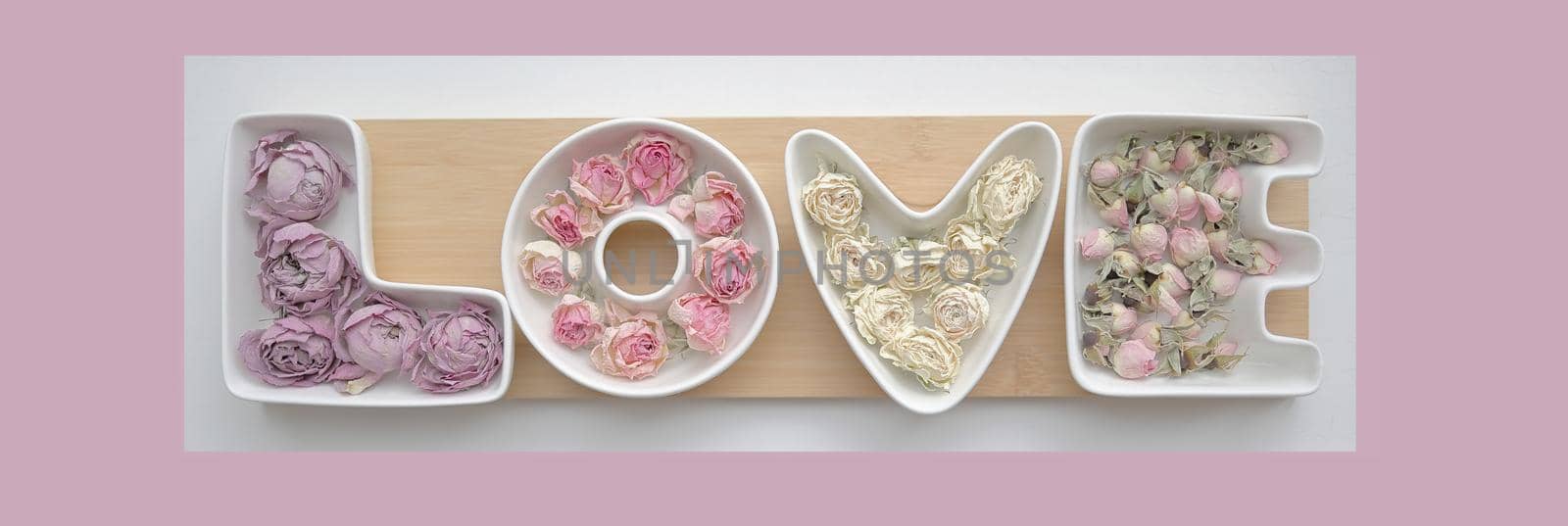Valentine's day and love concept. The word love is made up of white porcelain molds filled with rosebuds against a soft delicate pink background