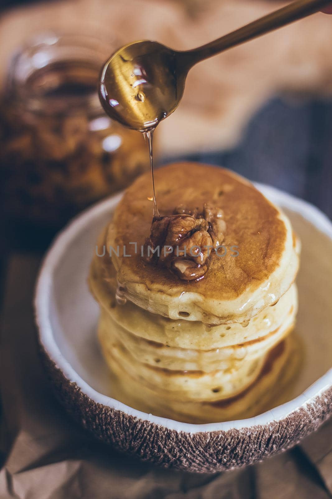 Stack of delicious pancakes with honey, nuts on wooden background.