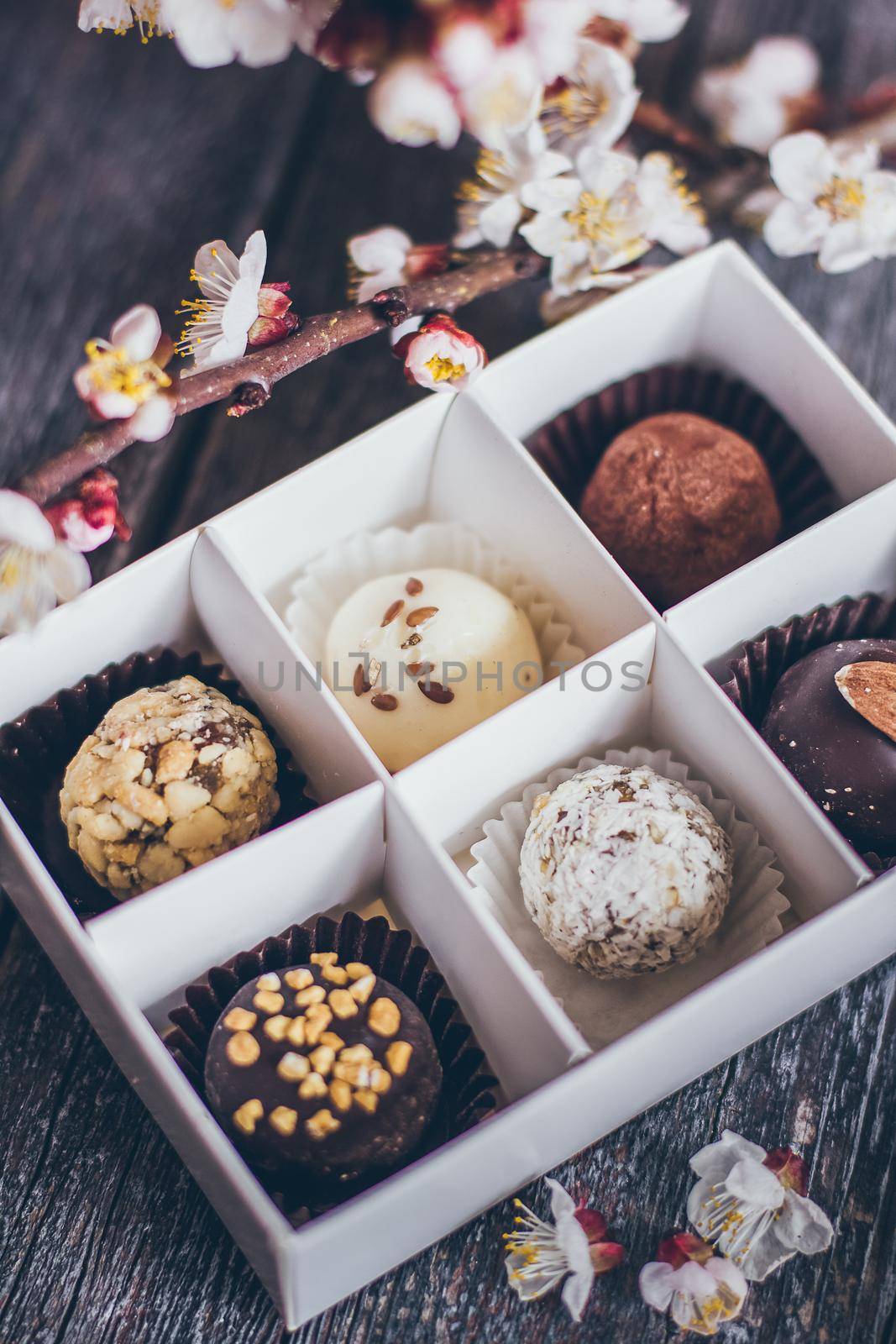 Spring collection of handmade chocolate bonbons candies and cherry flowers decoration on rustic wooden background.