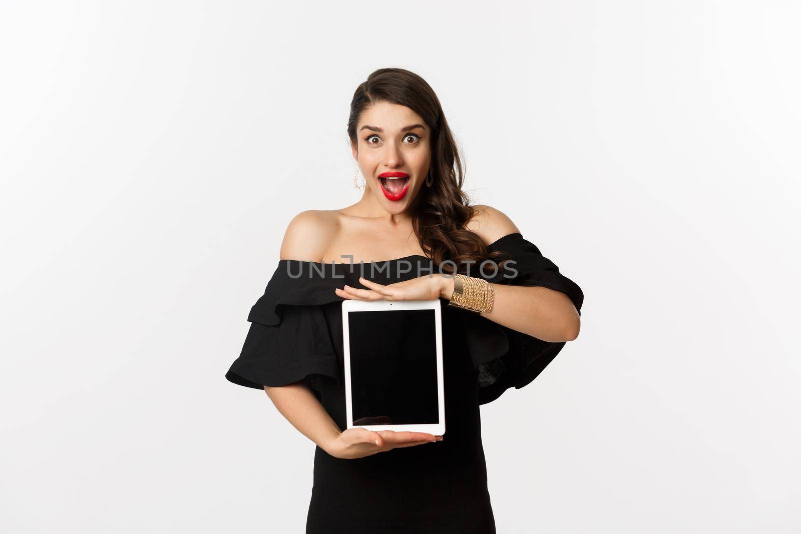 Fashion and shopping concept. Amazed young woman showing online website promo offer on tablet screen, looking excited camera, standing in black dress, white background by Benzoix