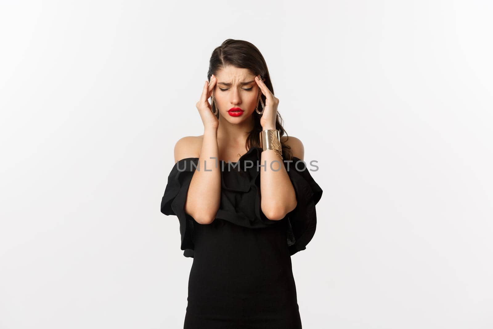 Fashion and beauty. Young modern woman in black dress, red lipstick, having headache, touching head and feeling sick, standing over white background.