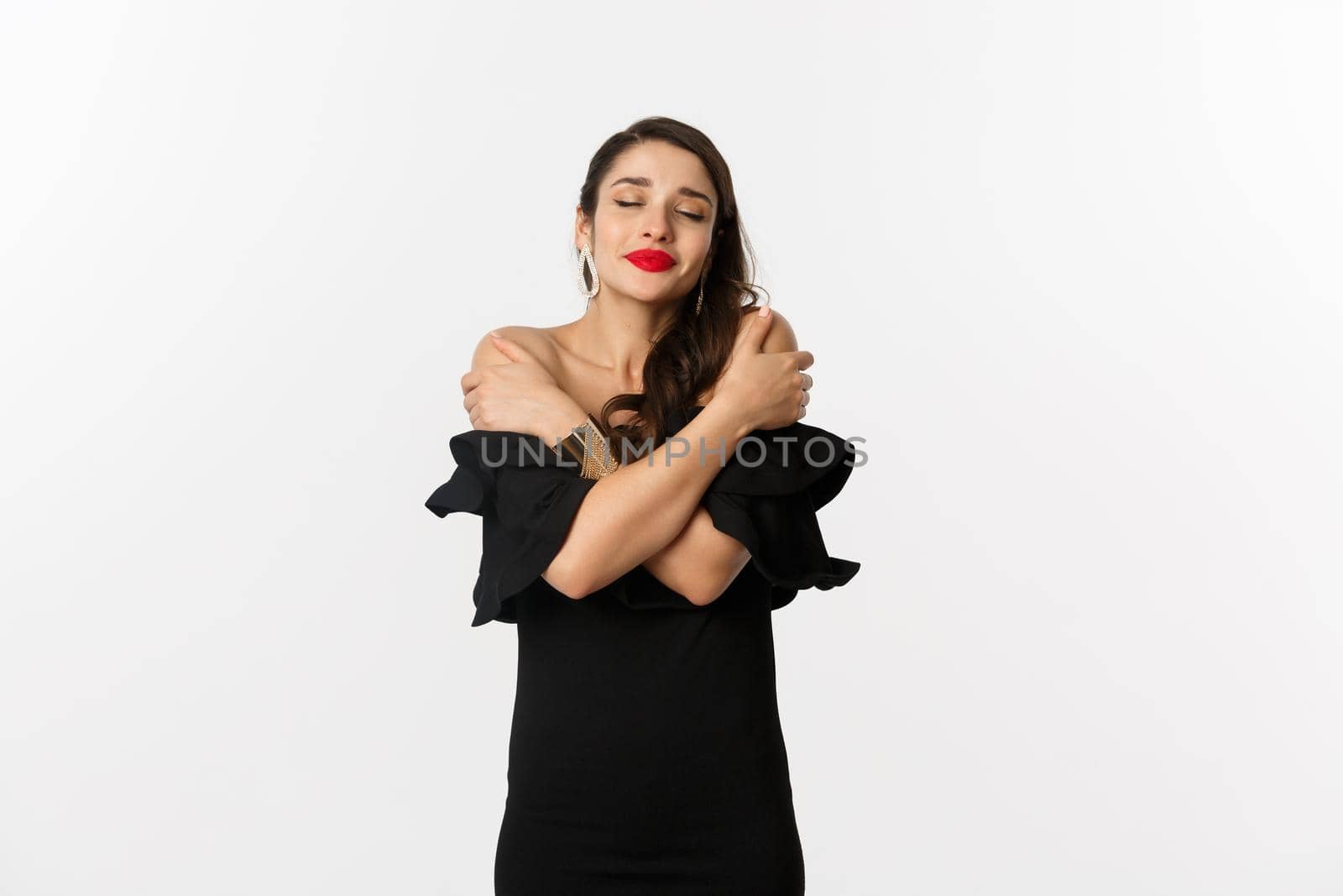 Fashion and beauty. Sensual and beautiful woman in black dress, hugging herself with closed eyes, daydreaming, standing over white background by Benzoix