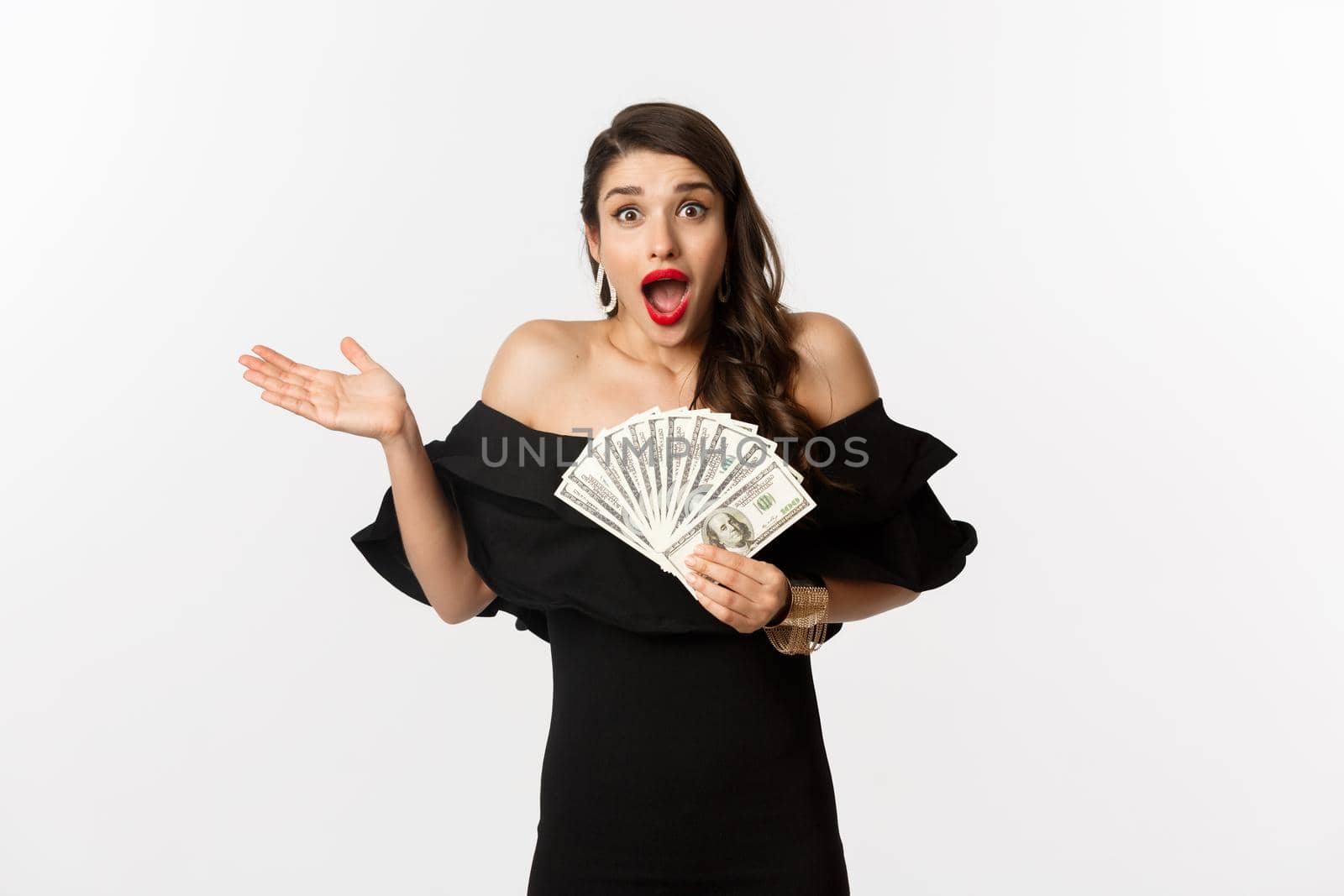 Beauty and shopping concept. Excited lucky woman winning money, looking amazed and holding dollars, standing over white background.