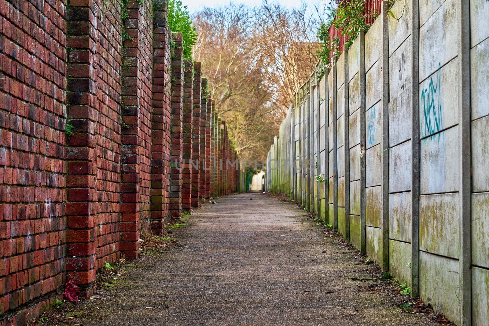 A brick wall on one side and concrete panels on the other. Looking down an urban alley.