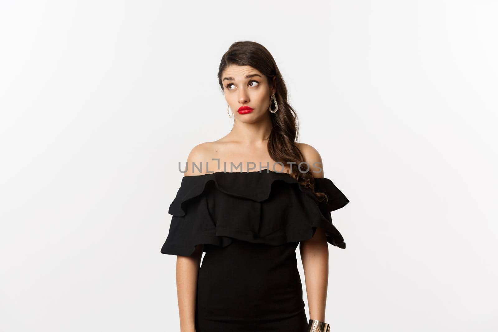 Fashion and beauty. Confused attractive woman in black dress, looking away with puzzled and shocked face, standing over white background.