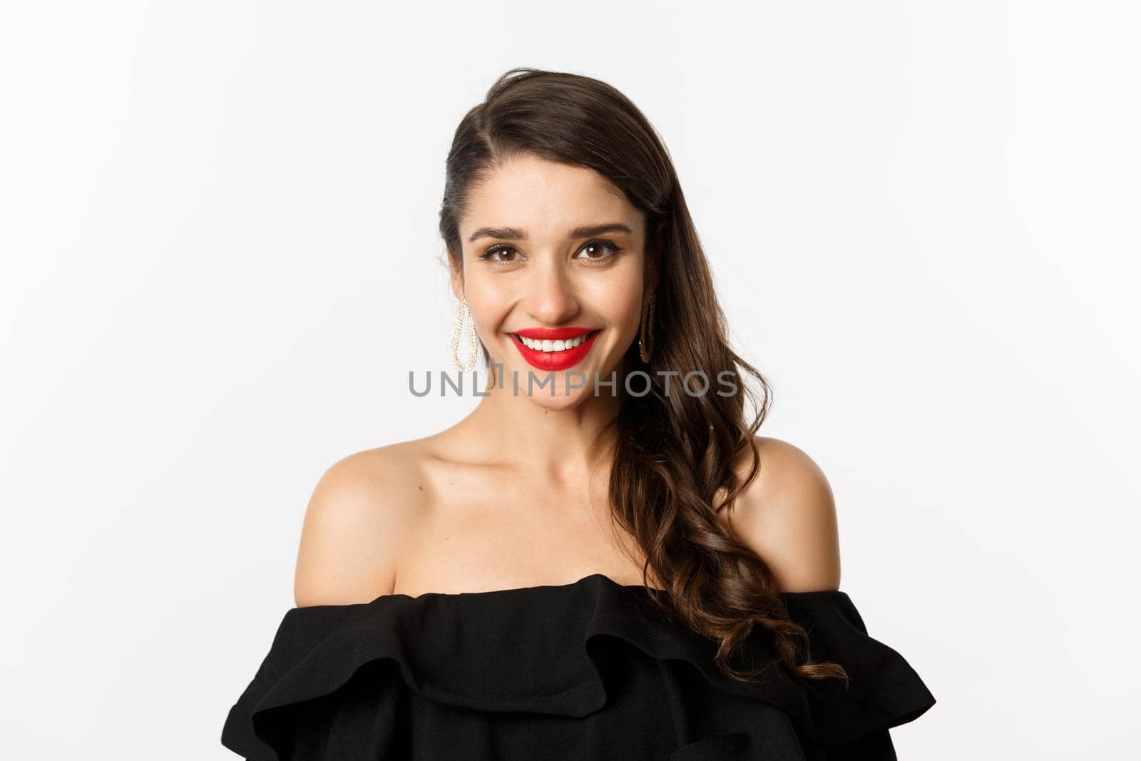 Close-up of beautiful woman dressed for party in black dress, wearing makeup and red lipstick, smiling happy at camera, white background.
