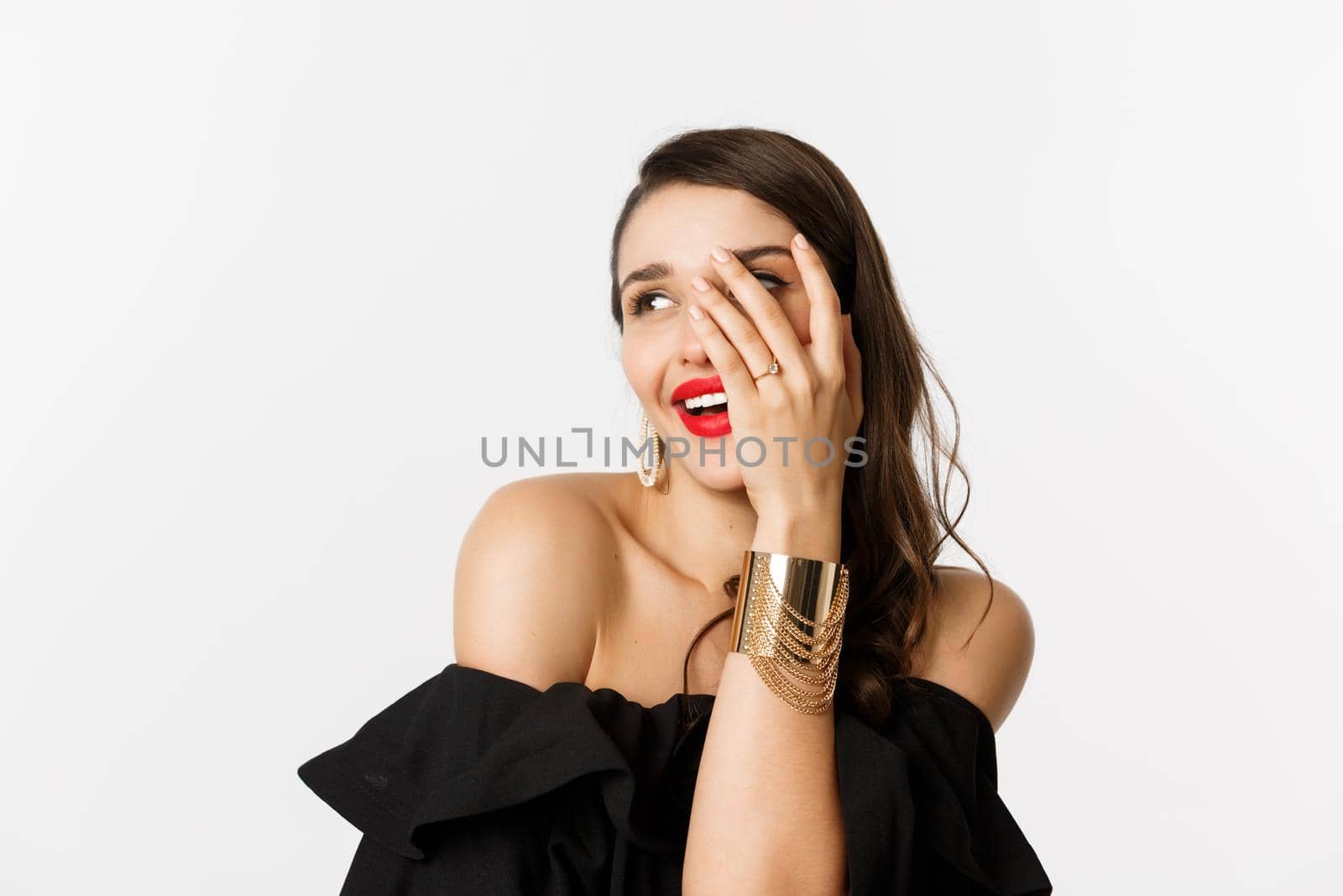 Close-up of beautiful woman show-off her engagement ring, showing hand and smiling coquettish, standing over white background by Benzoix