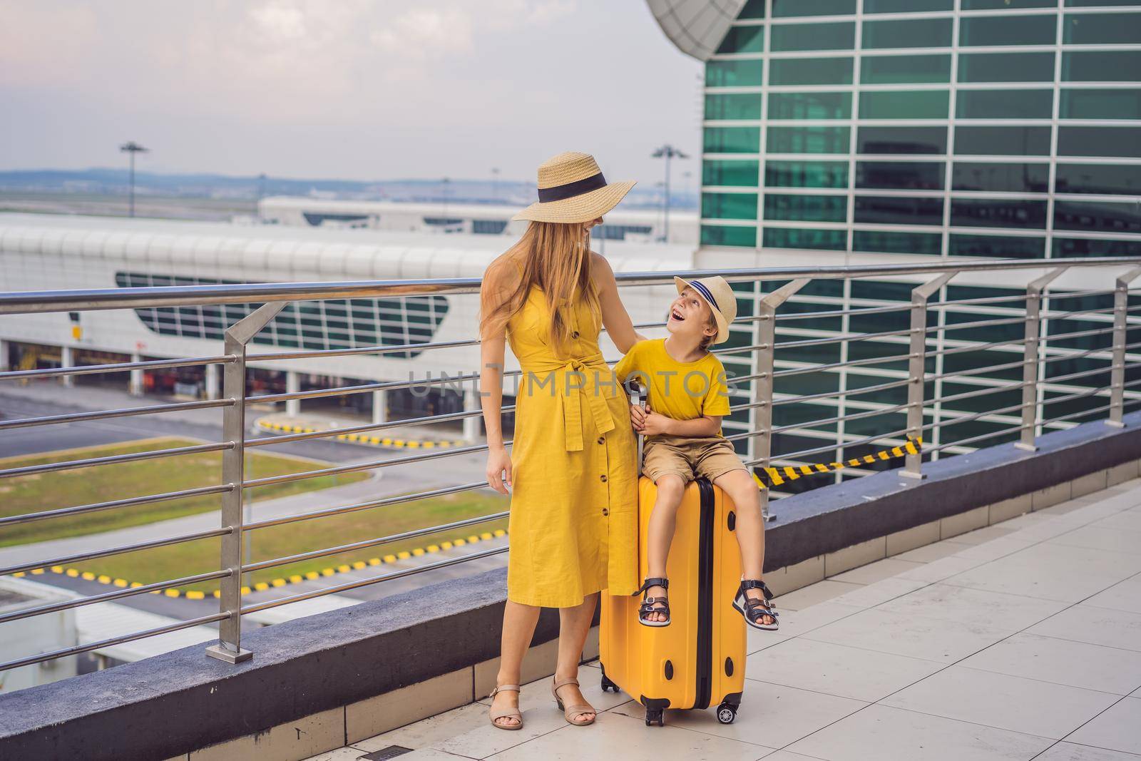 Family at airport before flight. Mother and son waiting to board at departure gate of modern international terminal. Traveling and flying with children. Mom with kid boarding airplane. yellow family look.