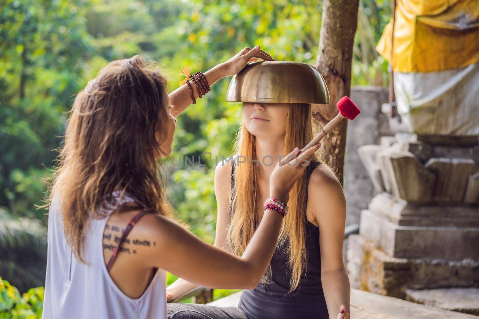 Nepal Buddha copper singing bowl at spa salon. Young beautiful woman doing massage therapy singing bowls in the Spa against a waterfall. Sound therapy, recreation, meditation, healthy lifestyle and body care concept by galitskaya