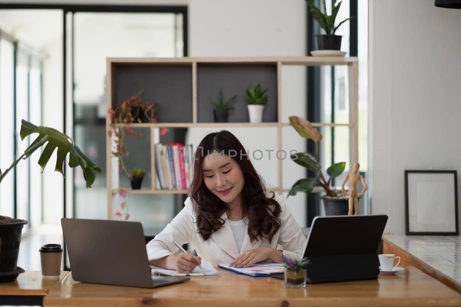 Portrait of young asian woman sitting at her desk with laptop and taking notes. Asian businesswoman working in modern office.