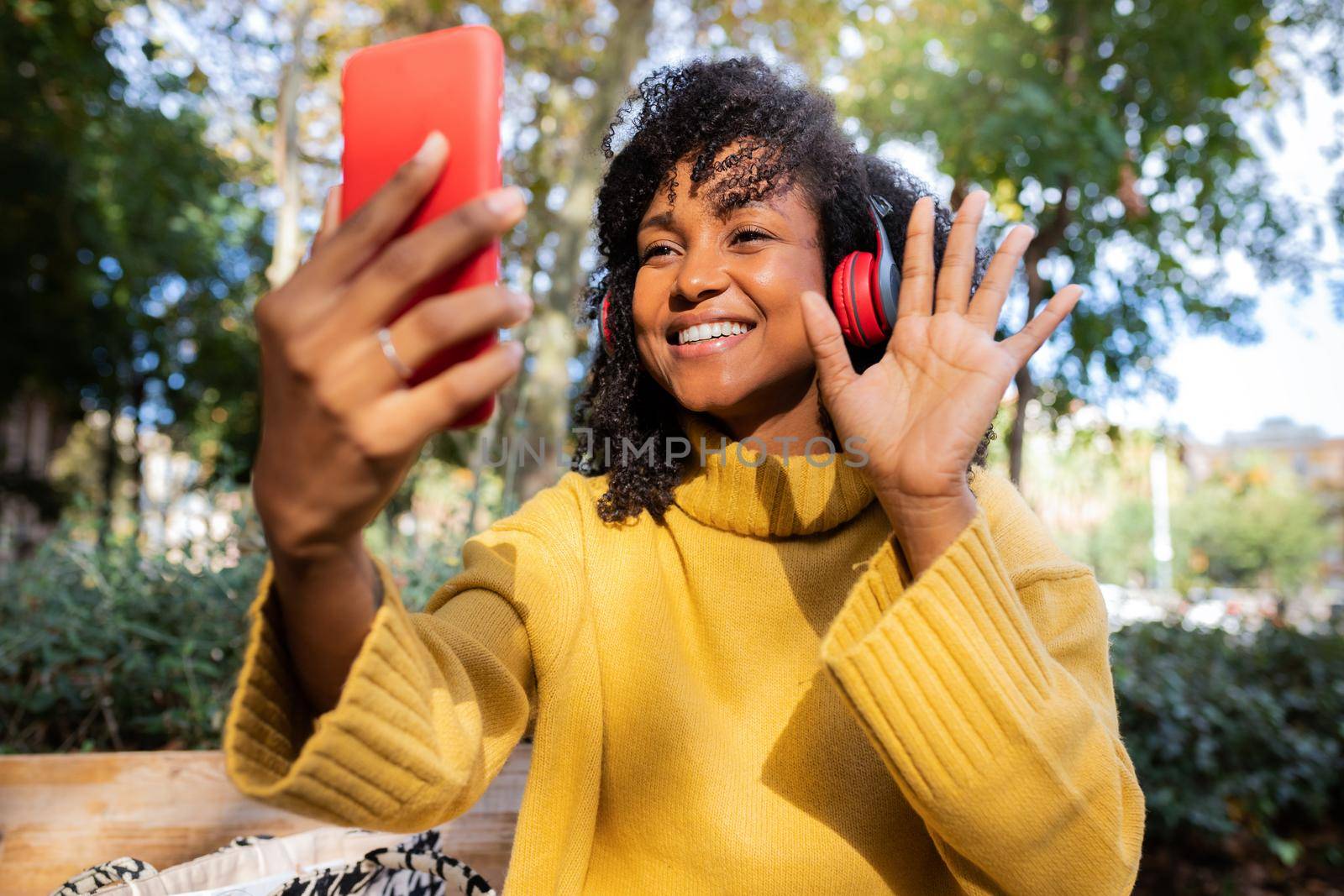 Smiling young African American woman wave hand on video call using mobile phone outdoors. Lifestyle and technology concept.