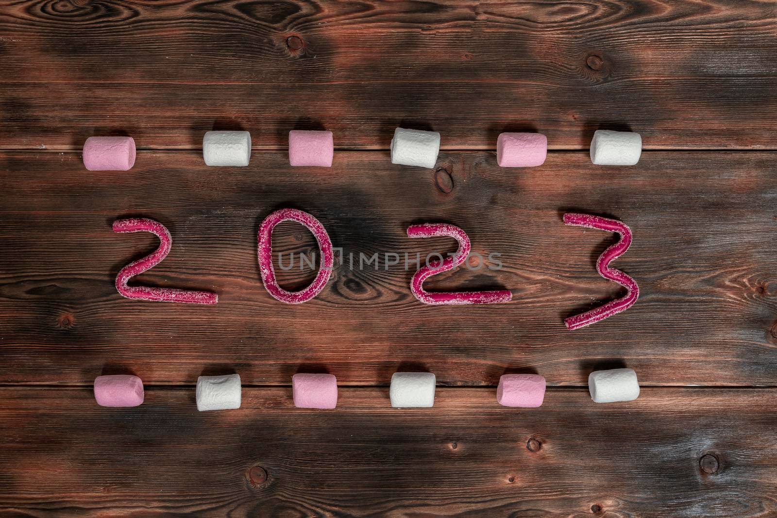 text 2023 from jelly marmalade surrounded by marshmallows on a wooden background.