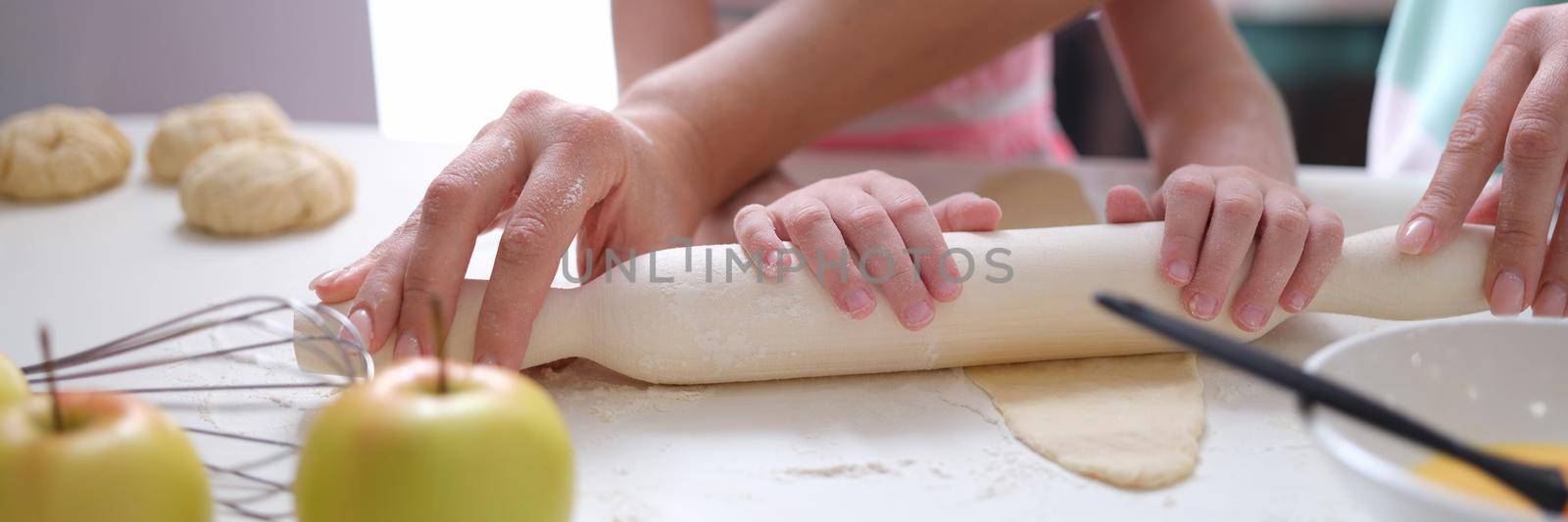 Adult and child roll out dough with rolling pin on table. Cooking classes and workshops for children concept