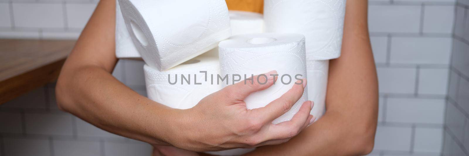 Woman holding many rolls of toilet paper in bathroom. Choosing toilet paper for home concept