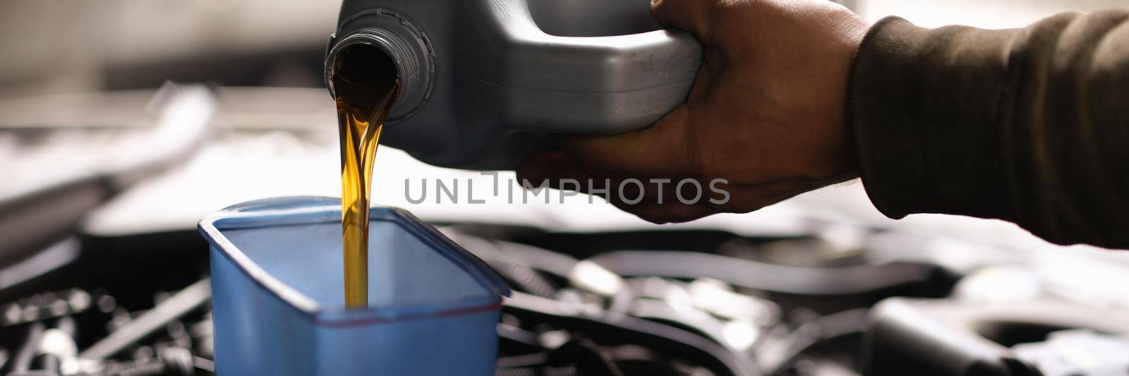 Foreman pours car oil into engine through watering can. Engine oil change intervals concept