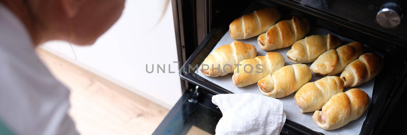 Woman takes out baking sheet of cooked croissants from oven. Cooking flour products at home concept